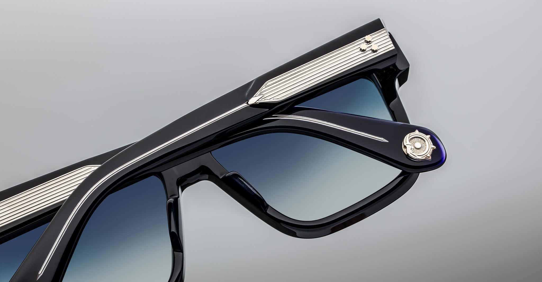 Close-up of stylish black sunglasses with metallic accents on the frames and a gradient blue tint on the lenses, set against a neutral gray background.