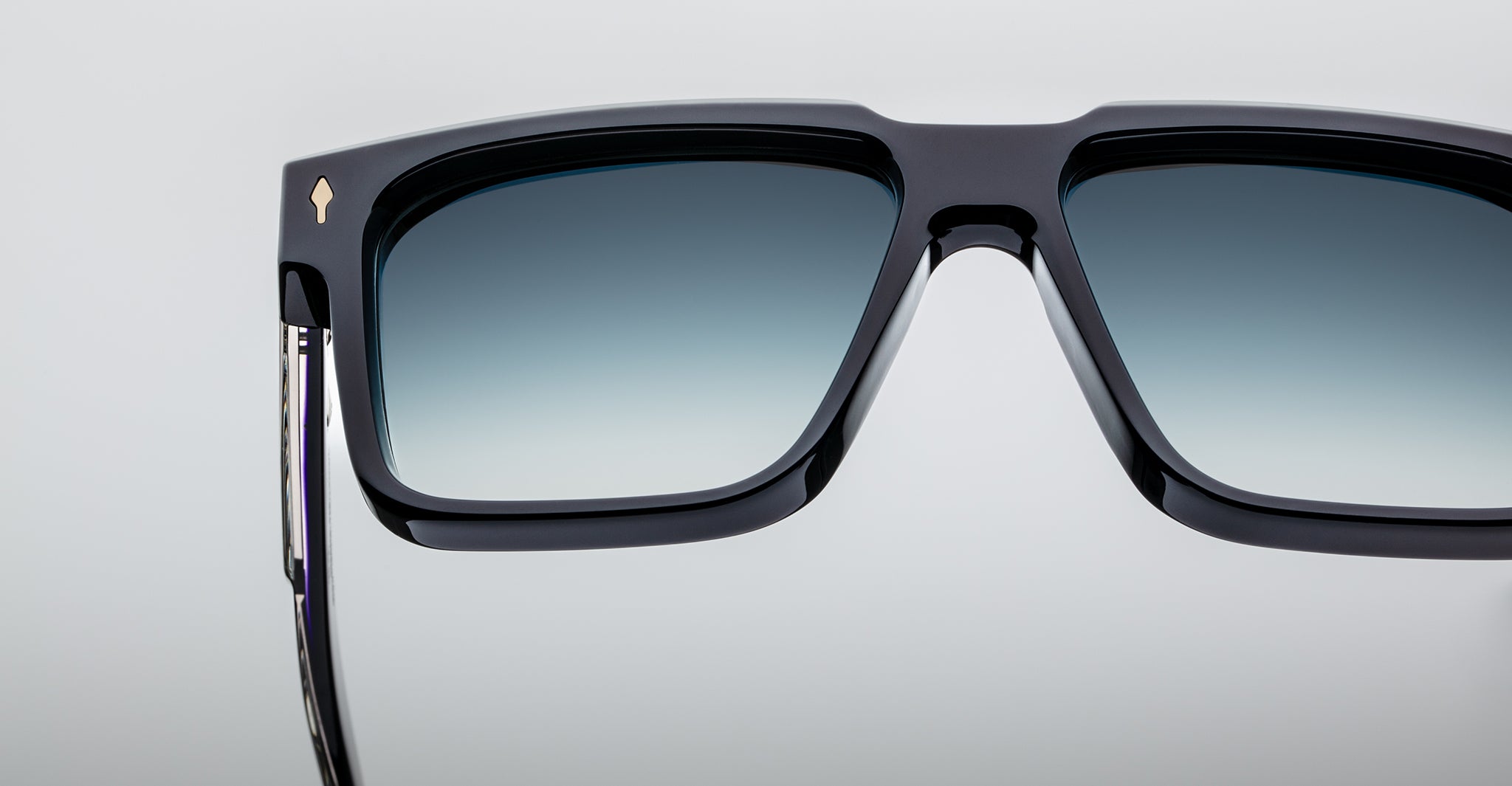 Close-up of black rectangular sunglasses with gradient blue-tinted lenses, against a plain light background. Only the upper half and temples of the sunglasses are visible.