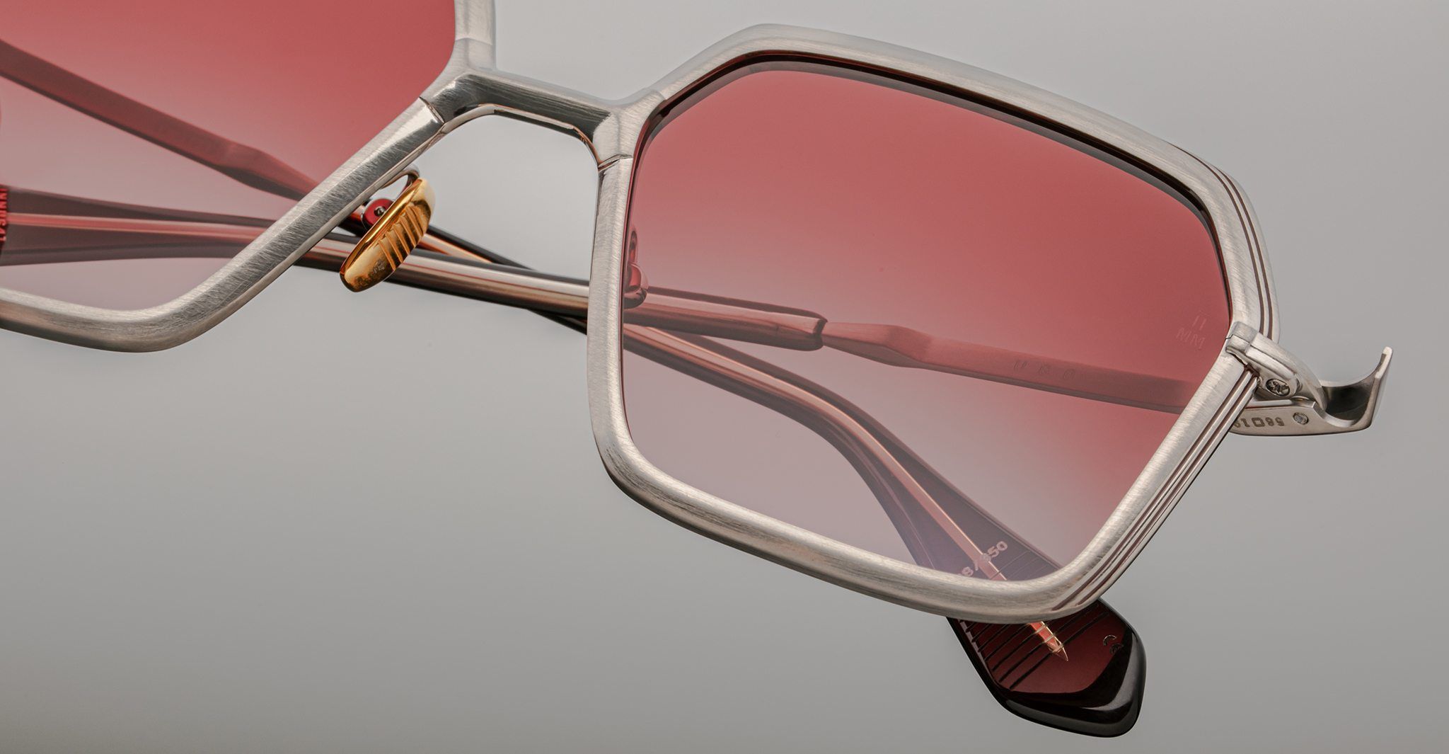 Close-up of Jacques Marie Mage Ugo eyeglasses featuring a metallic silver frame and large, geometric pink-tinted lenses, set against a plain light gray background.