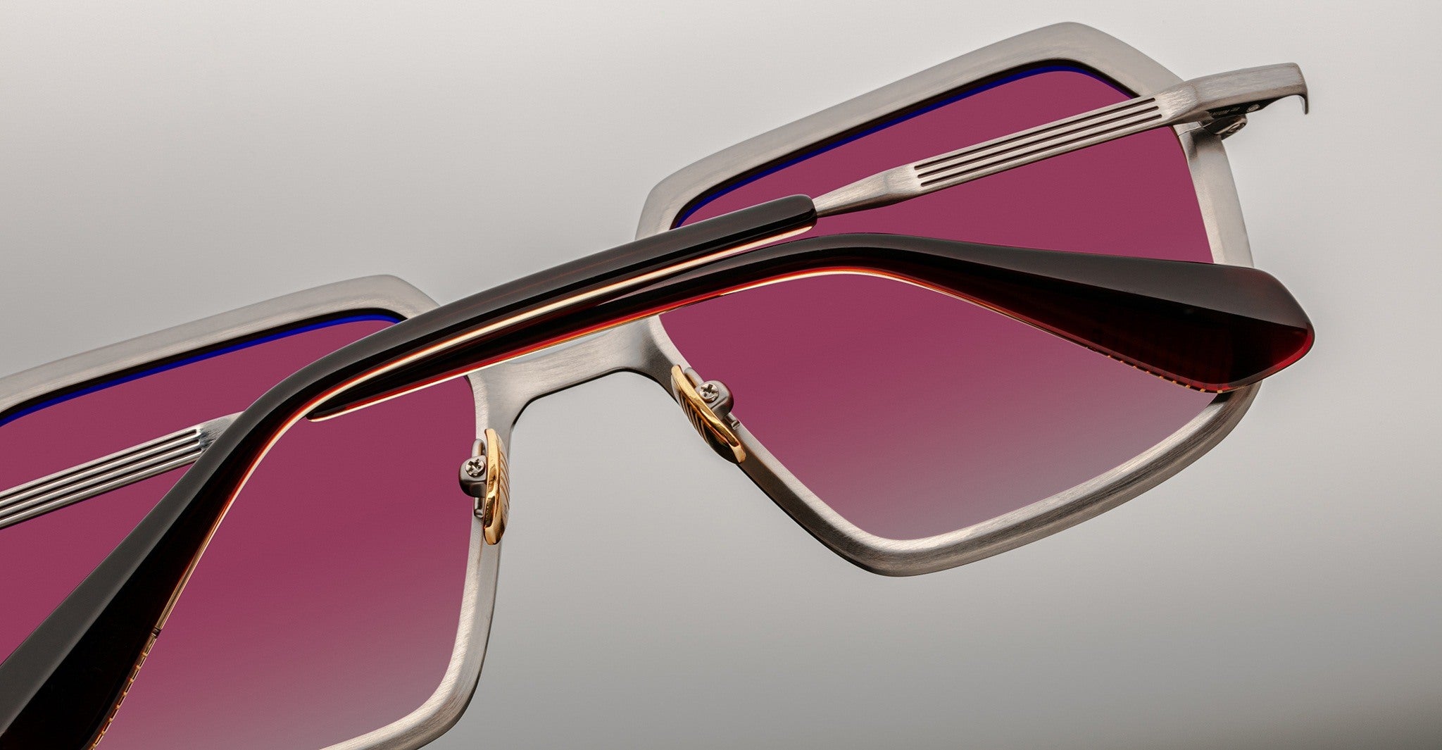 Close-up view of Jacques Marie Mage Ugo rectangular sunglasses featuring silver frames, red gradient lenses, and black and red arms. The image highlights detailed craftsmanship in the lenses, frames, and arm design.