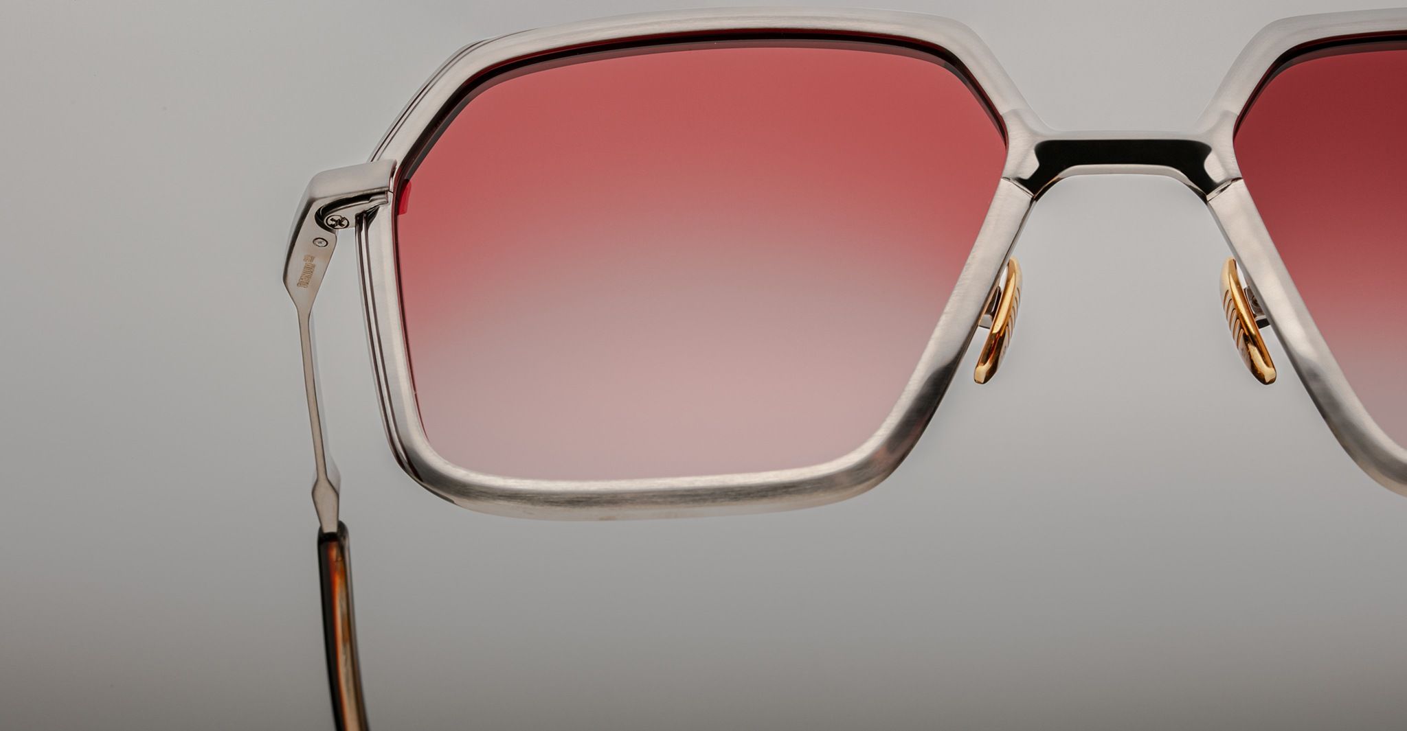 A close-up of the upper half of Jacques Marie Mage Ugo sunglasses featuring large hexagonal silver frames and gradient pink lenses against a plain background.