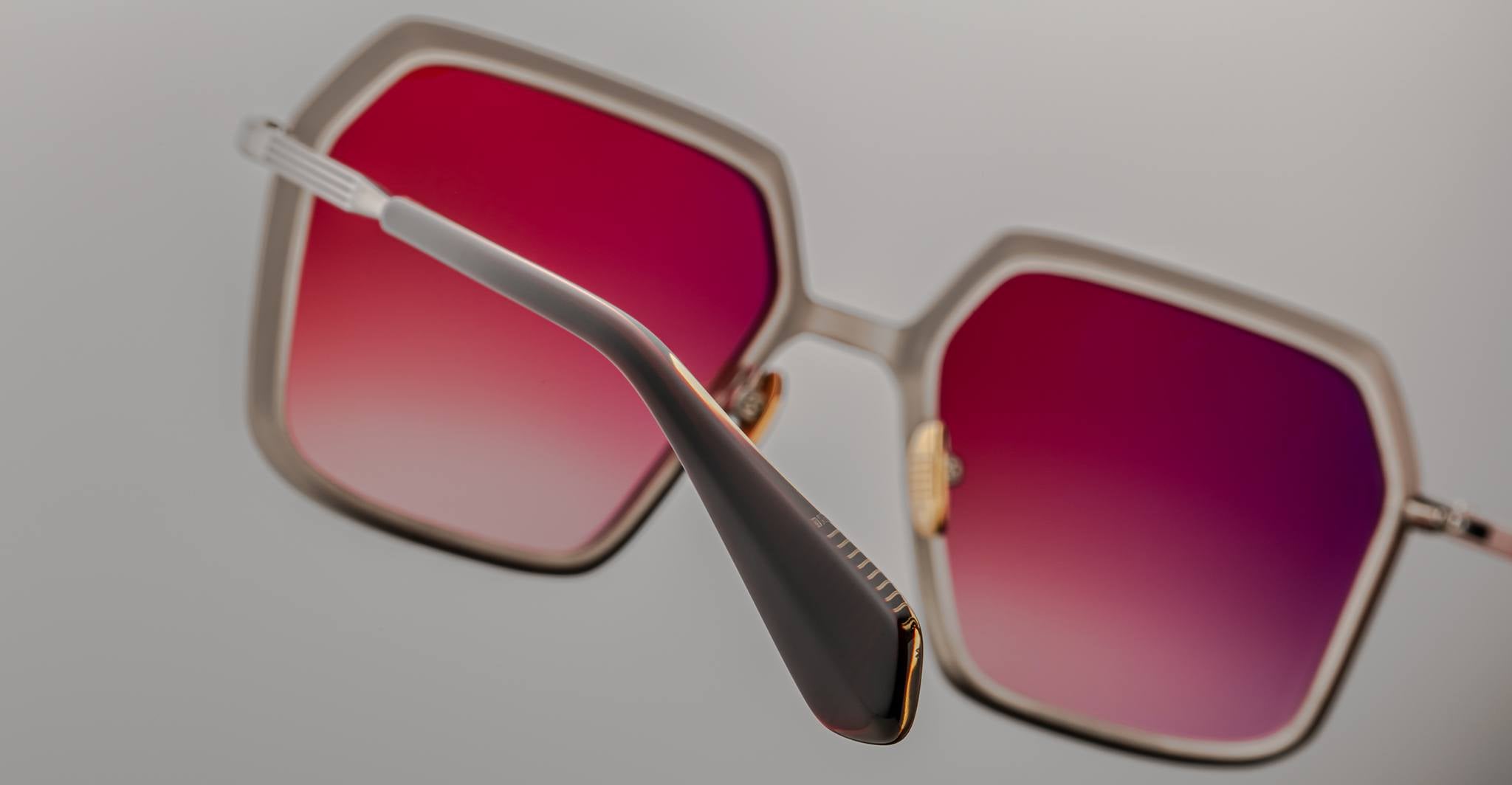 A close-up of the Jacques Marie Mage Ugo square sunglasses, featuring gradient pink lenses and thin metal frames, shown from the side and slightly above against a plain background.