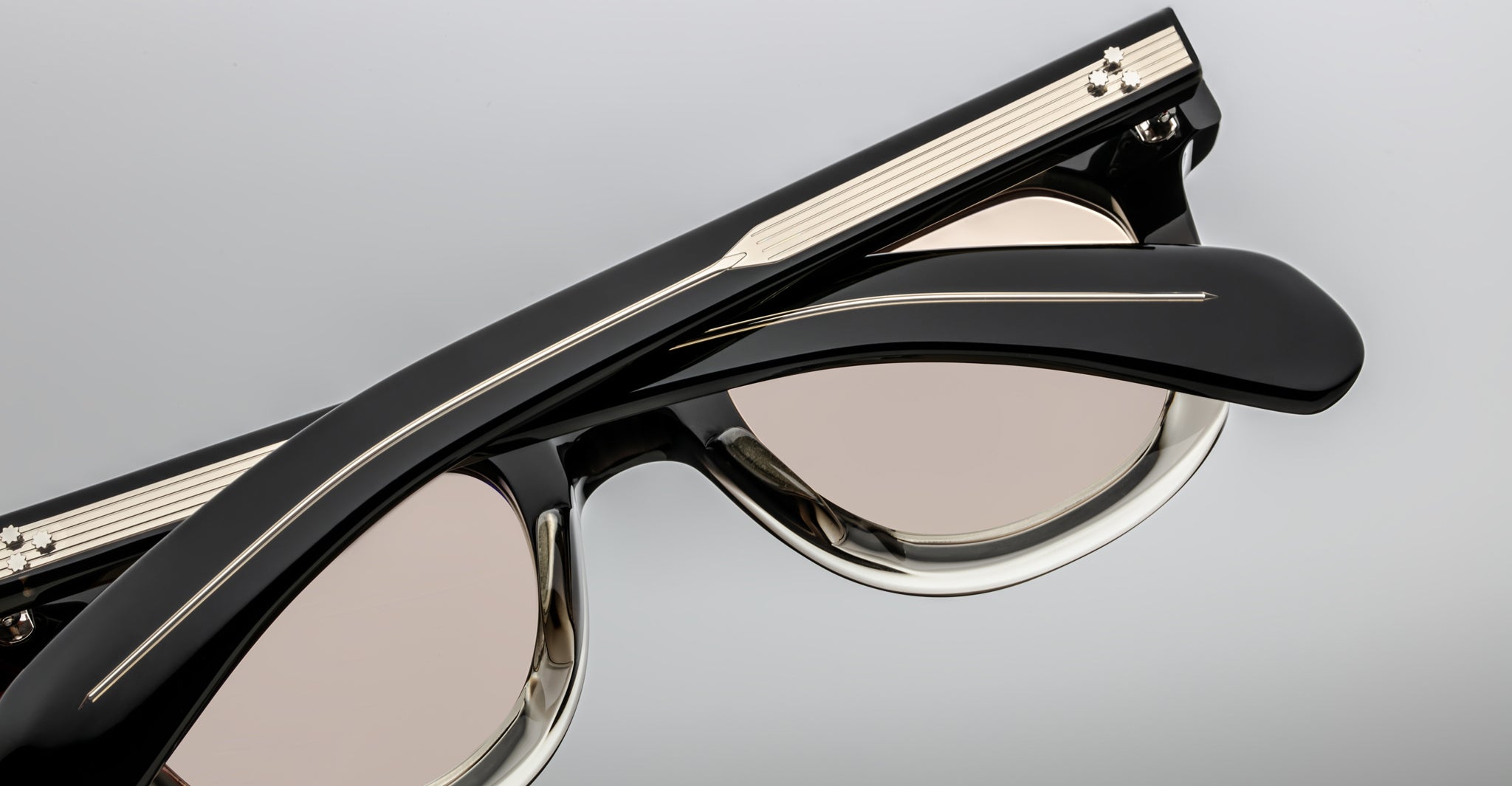 Close-up of Jacques Marie Mage Vendome sunglasses in black with beige-tinted lenses and silver arm details, handcrafted in Japan, shown folded against a light background.