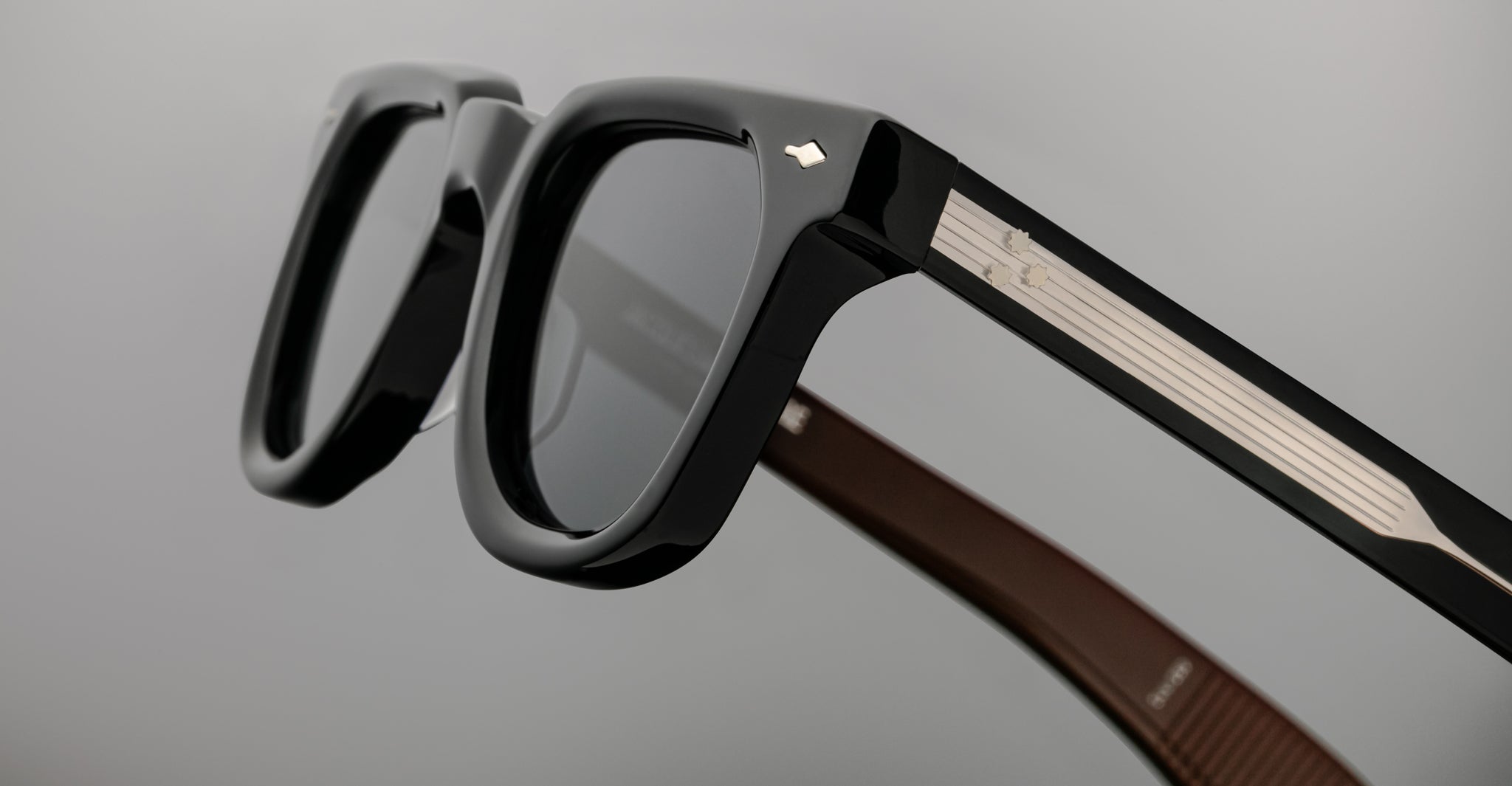 Close-up of Jacques Marie Mage Vendome black optical frames featuring thick rims and silver temple accents, set against a plain gray background. Expertly handcrafted in Japan by Jacques Marie Mage.