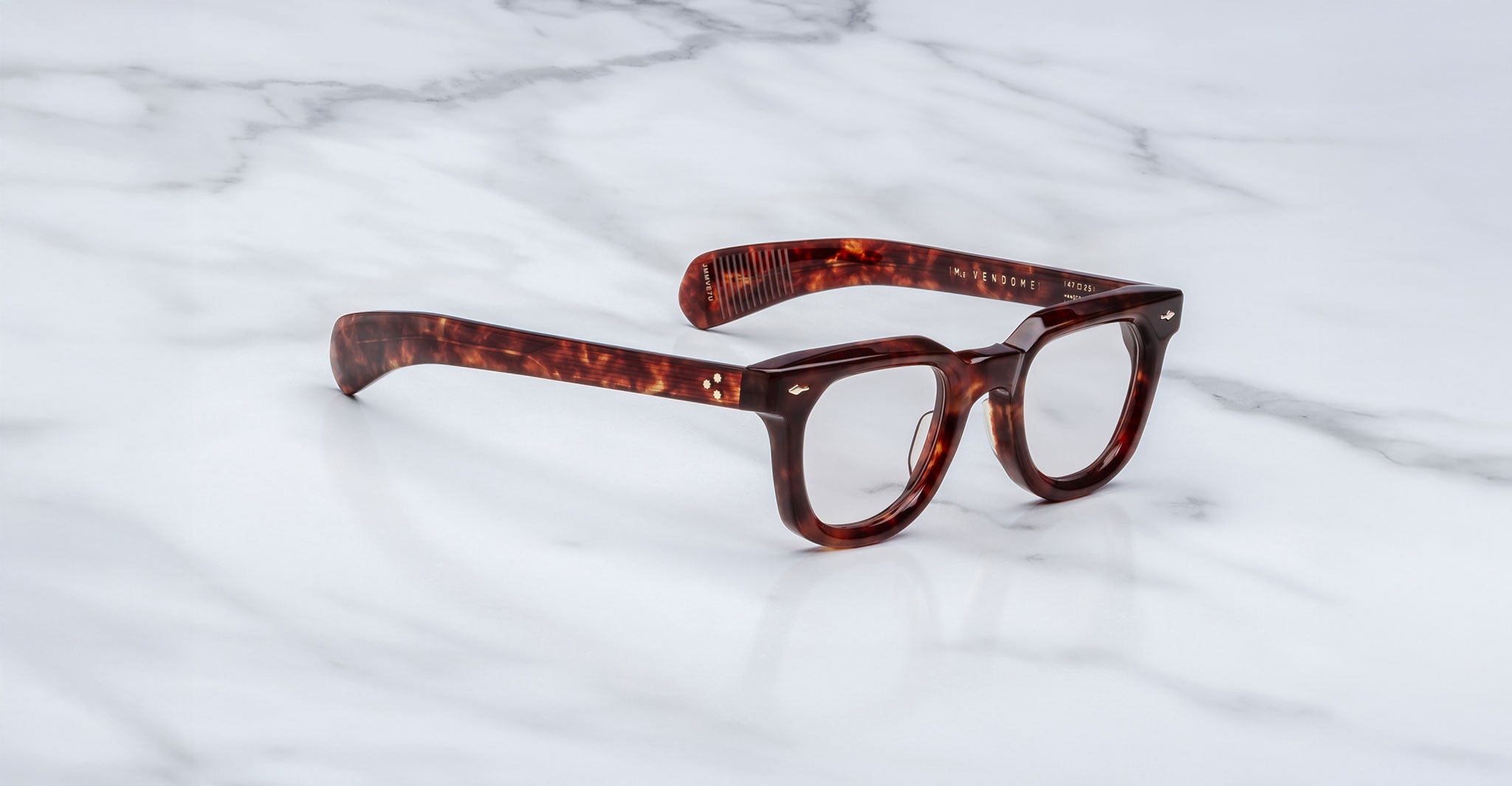 A pair of Jacques Marie Mage Vendome optical frames by Jacques Marie Mage, featuring a thick tortoiseshell design and clear lenses, rests on a white marble surface.