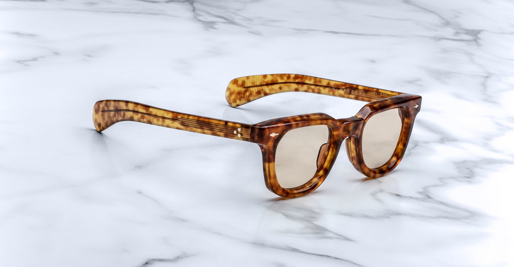 A pair of Jacques Marie Mage Vendome sunglasses by Jacques Marie Mage, featuring brown tortoiseshell thick frames, handcrafted in Japan, displayed on a white marble surface.