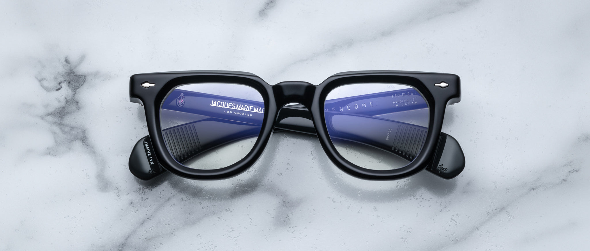 Jacques Marie Mage Vendome eyeglasses with text reflected in lenses, shown from above on a white marble surface.