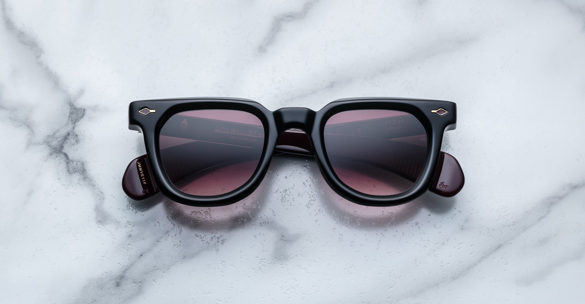 Jacques Marie Mage Vendome black square sunglasses with dark lenses, handcrafted in Japan, rest on a white marble surface.