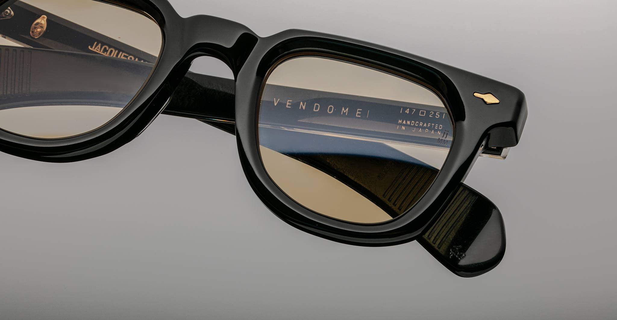 Close-up of Jacques Marie Mage Vendome optical frames in black with brown-tinted lenses. The inner temple bears a "handcrafted in Japan" label, highlighting the brand’s renowned quality and design.