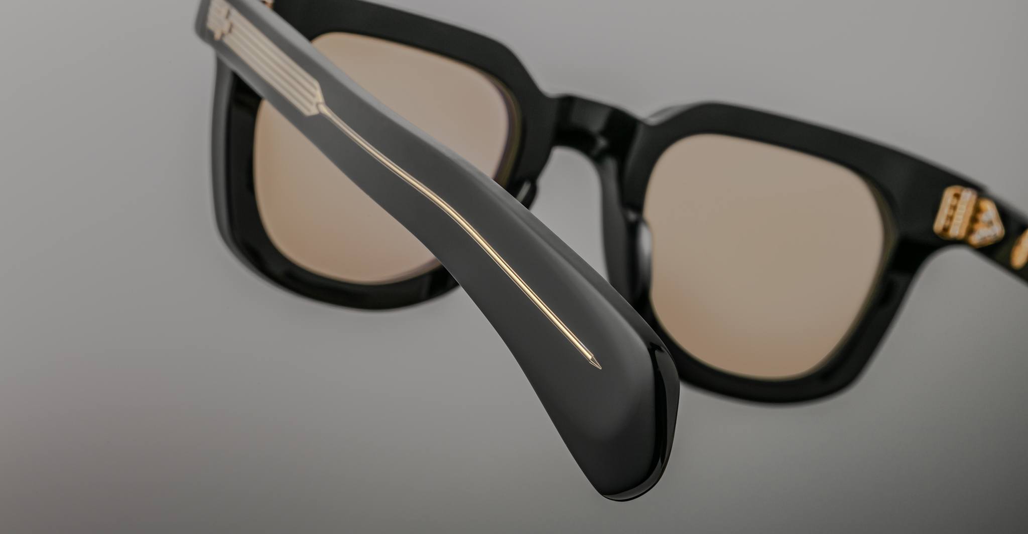 A close-up of Jacques Marie Mage Vendome sunglasses in black with tan lenses, featuring gold accents on the arm and a triangular logo by the hinge—expertly handcrafted in Japan.