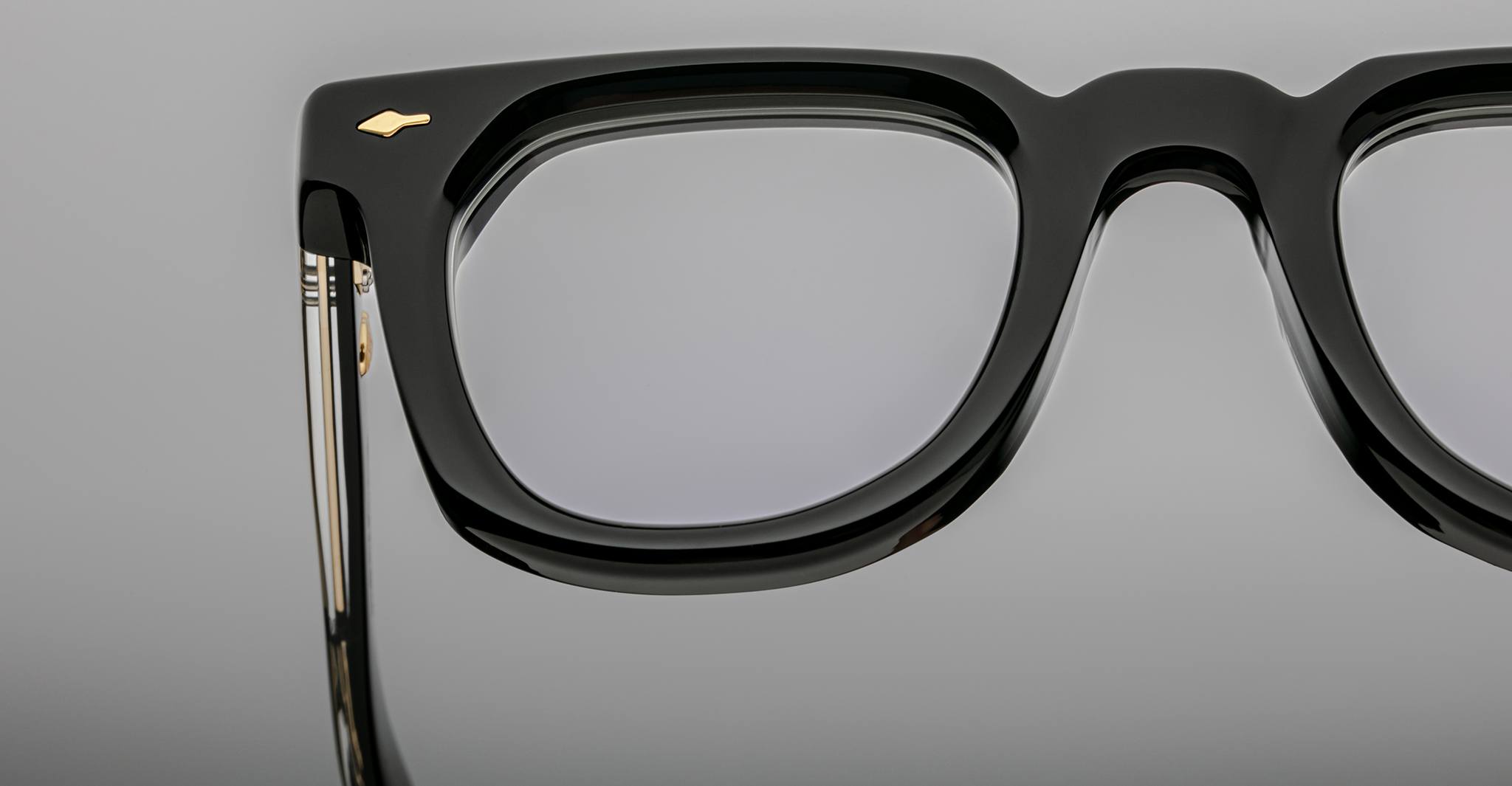 Close-up of the upper half of Jacques Marie Mage Vendome optical frames in black, handcrafted in Japan, with a gold accent by the hinge, shown against a plain gray background.