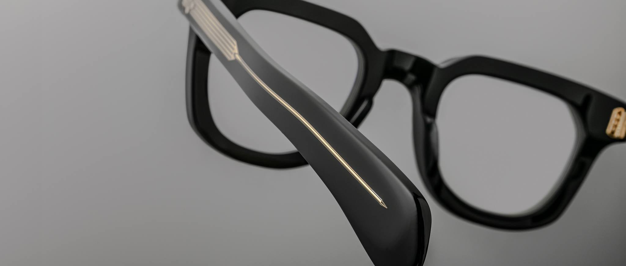 Close-up of Jacques Marie Mage Vendome eyeglasses, black thick frames, gold line detail on temple, viewed from the side.