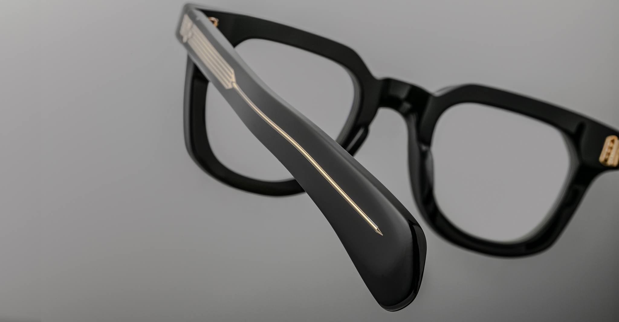 Close-up of Jacques Marie Mage Vendome optical frames in thick black Japanese acetate with gold temple detailing by Jacques Marie Mage, set against a plain gray background.