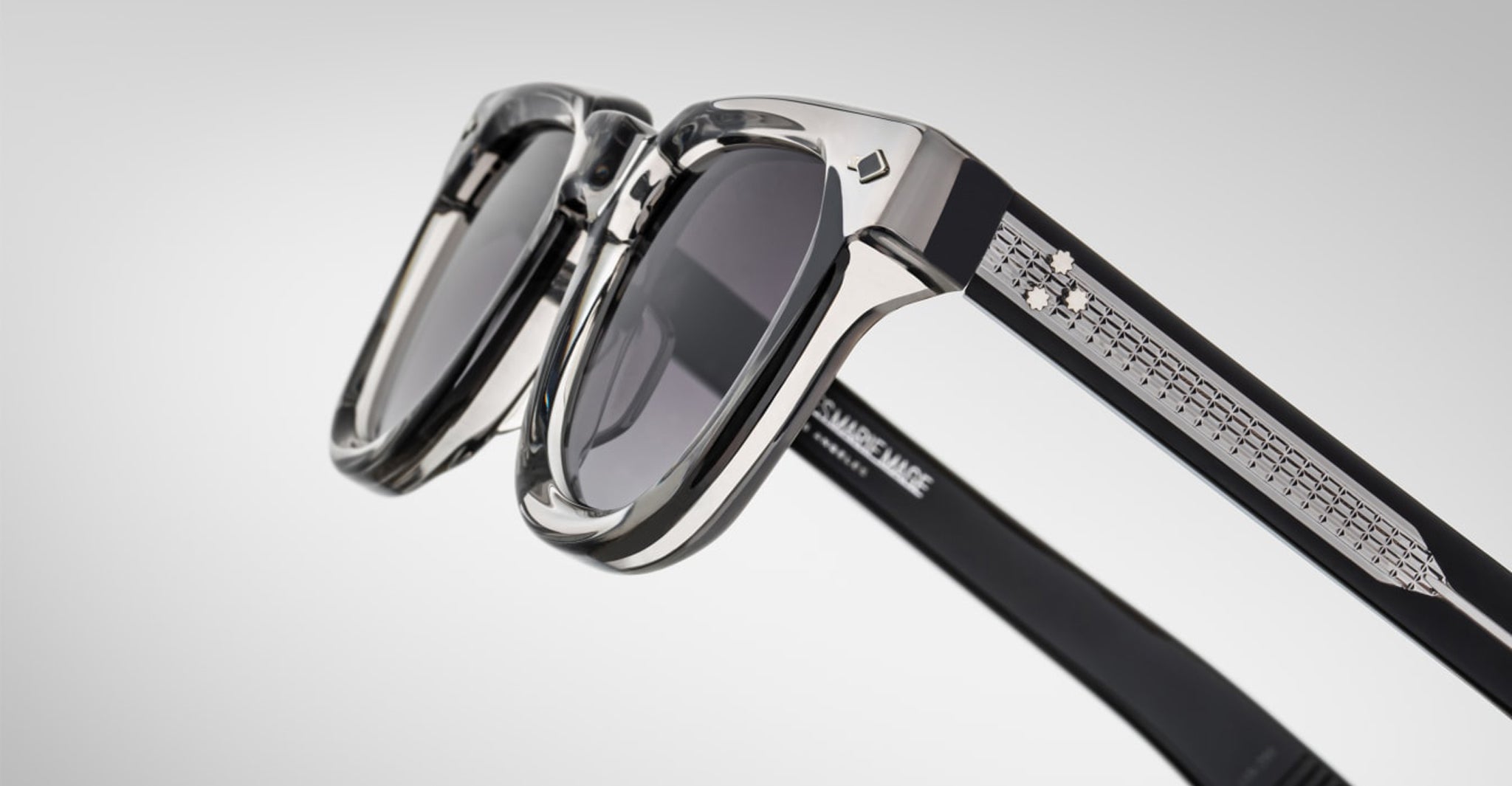 Close-up of Jacques Marie Mage Vendome sunglasses by Jacques Marie Mage, featuring black frames, clear rims, silver arm detailing, and handcrafted in Japan, set against a plain light background.