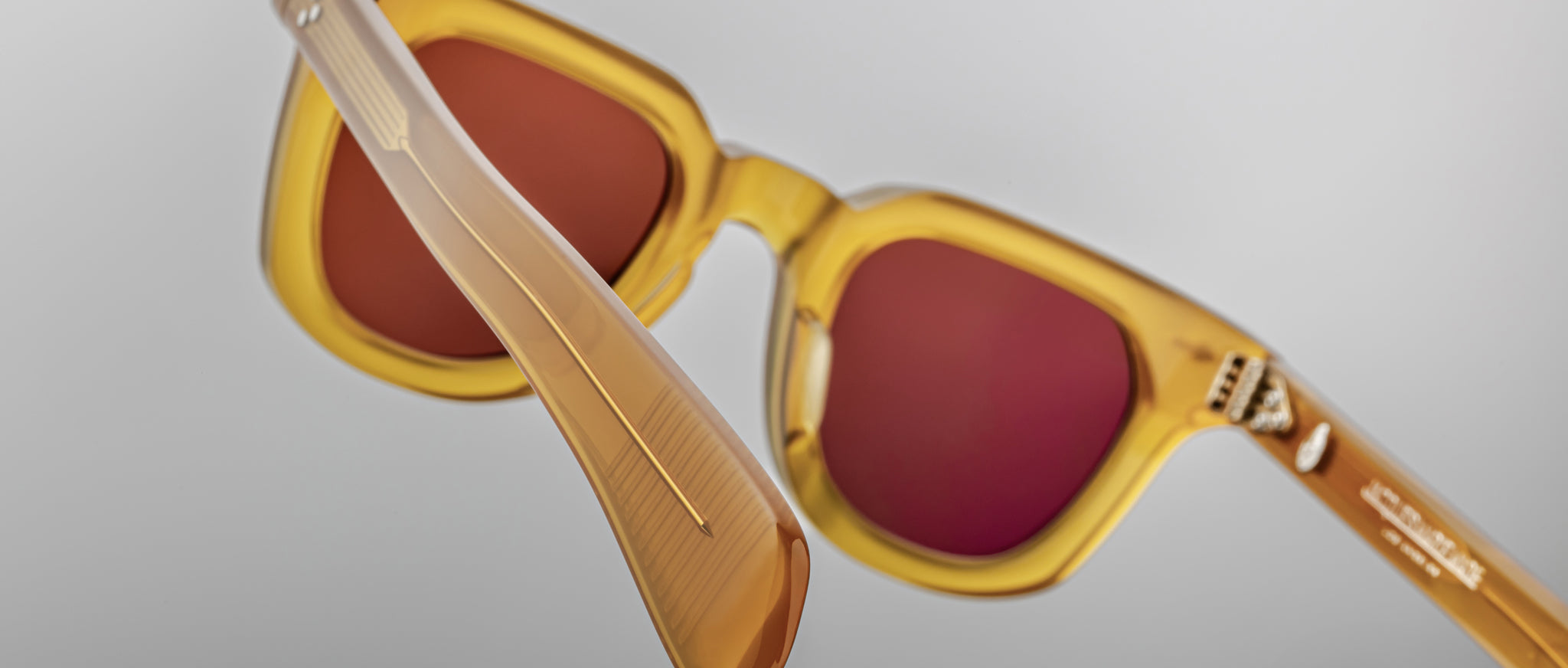 Close-up of Jacques Marie Mage Vendome sunglasses with amber frame and red lenses, viewed from the front.