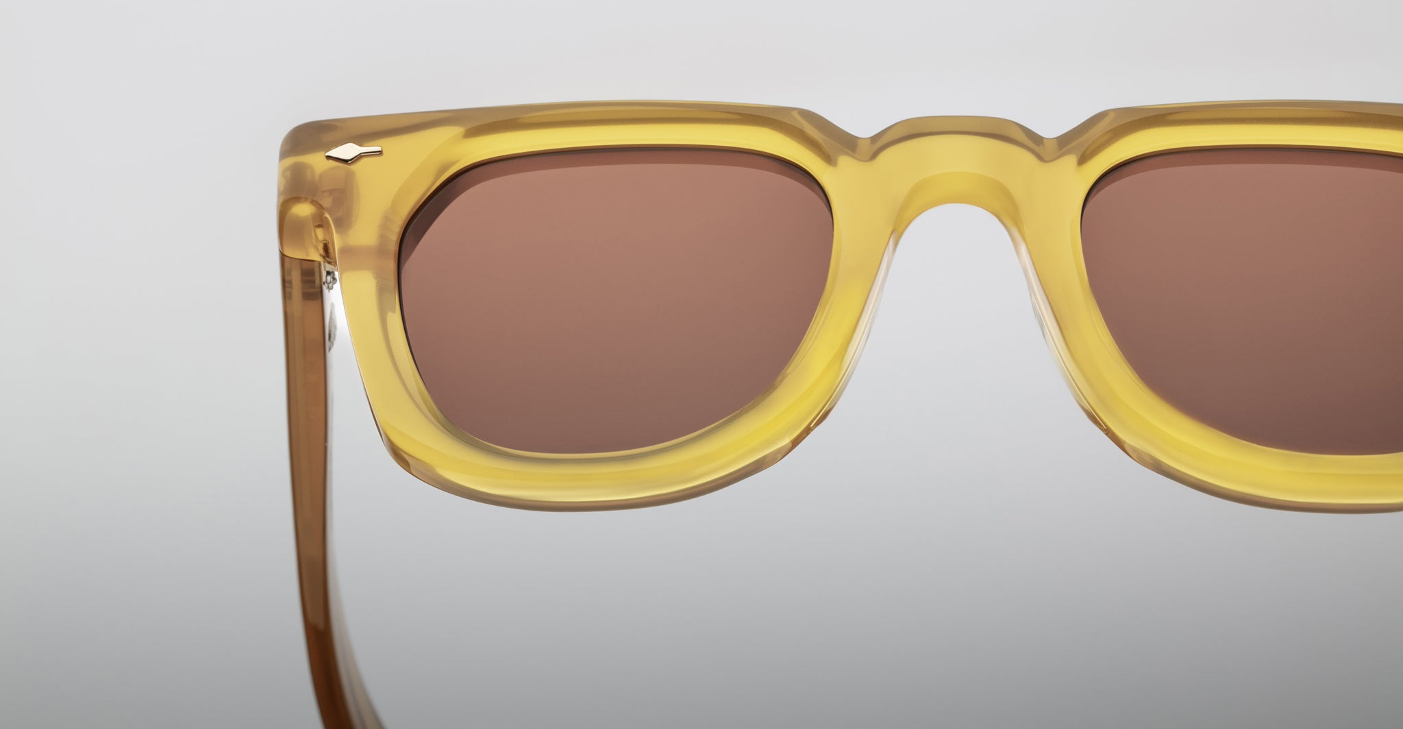 Close-up of Jacques Marie Mage Vendome sunglasses, featuring yellow translucent frames and brown lenses, showcasing the upper half and one arm. Expertly handcrafted in Japan by Jacques Marie Mage, set against a neutral background.