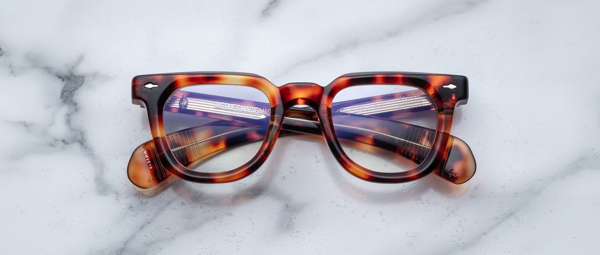 Jacques Marie Mage Vendome thick-frame eyeglasses, front view, displayed on a white marble surface.