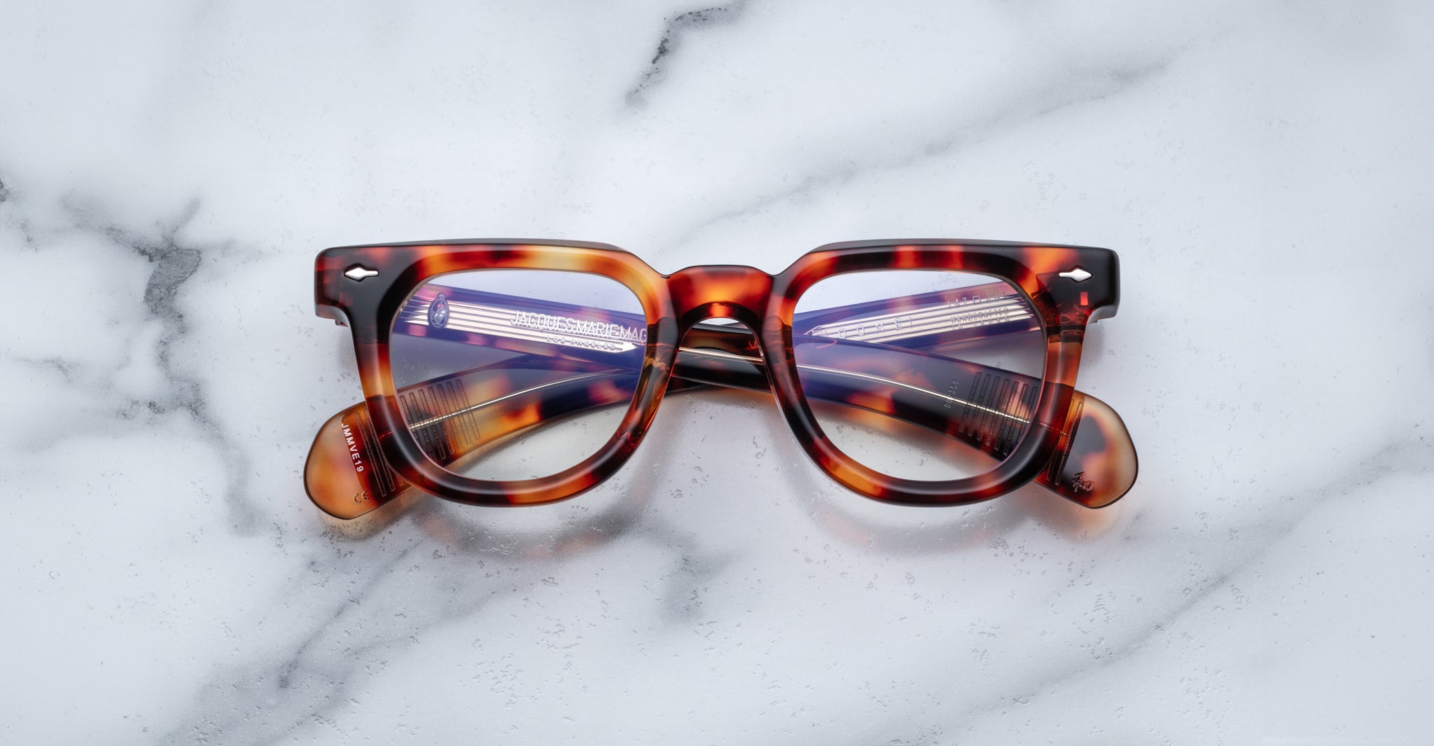 The Jacques Marie Mage Vendome by Jacques Marie Mage features handcrafted Japanese tortoiseshell optical frames with a rectangular design, displayed elegantly on a white marble surface.