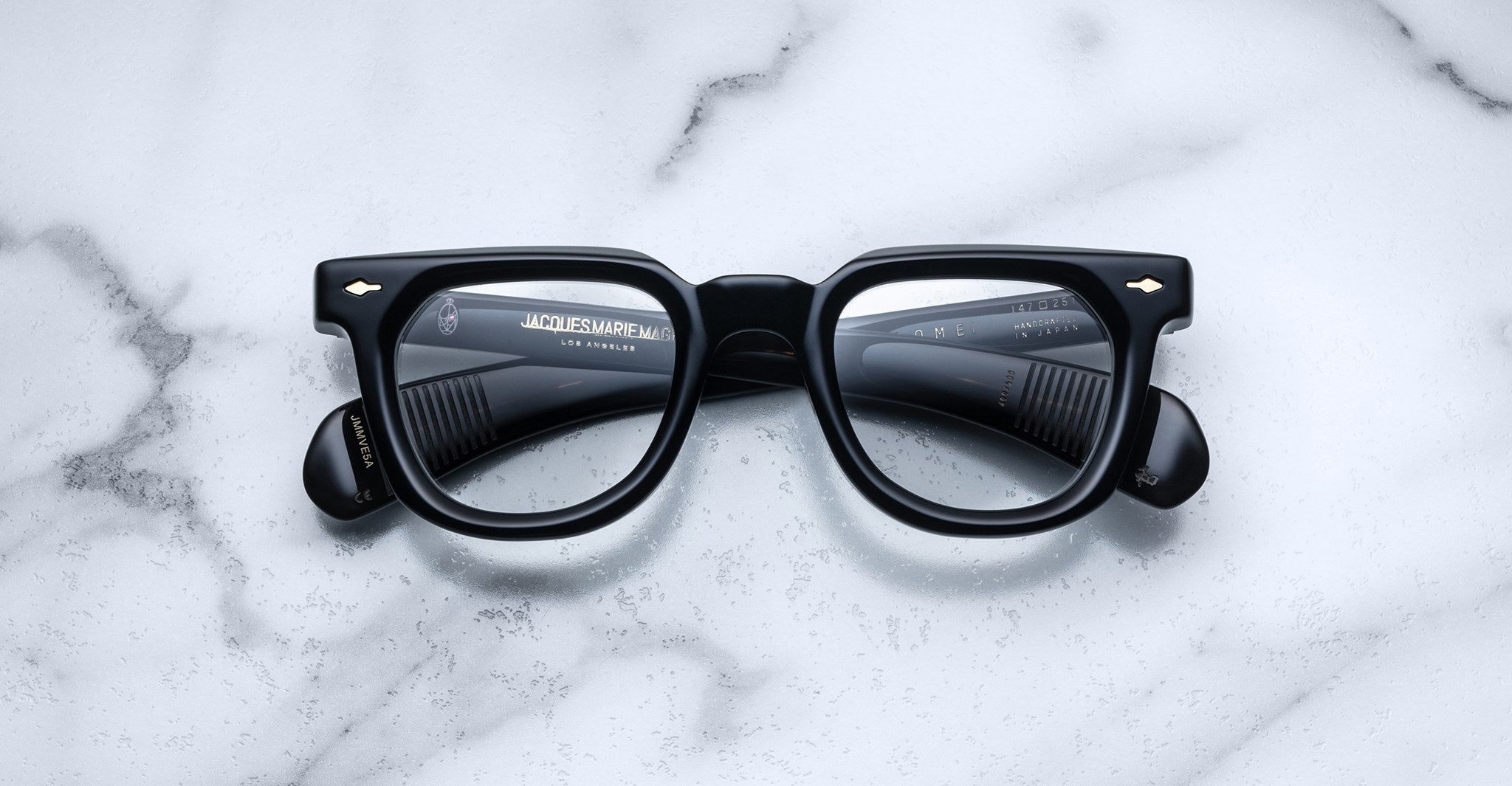 Jacques Marie Mage Vendome black rectangular optical frames by Jacques Marie Mage, featuring thick rims and handcrafted in Japan, are displayed elegantly on a white marble surface in an overhead view.