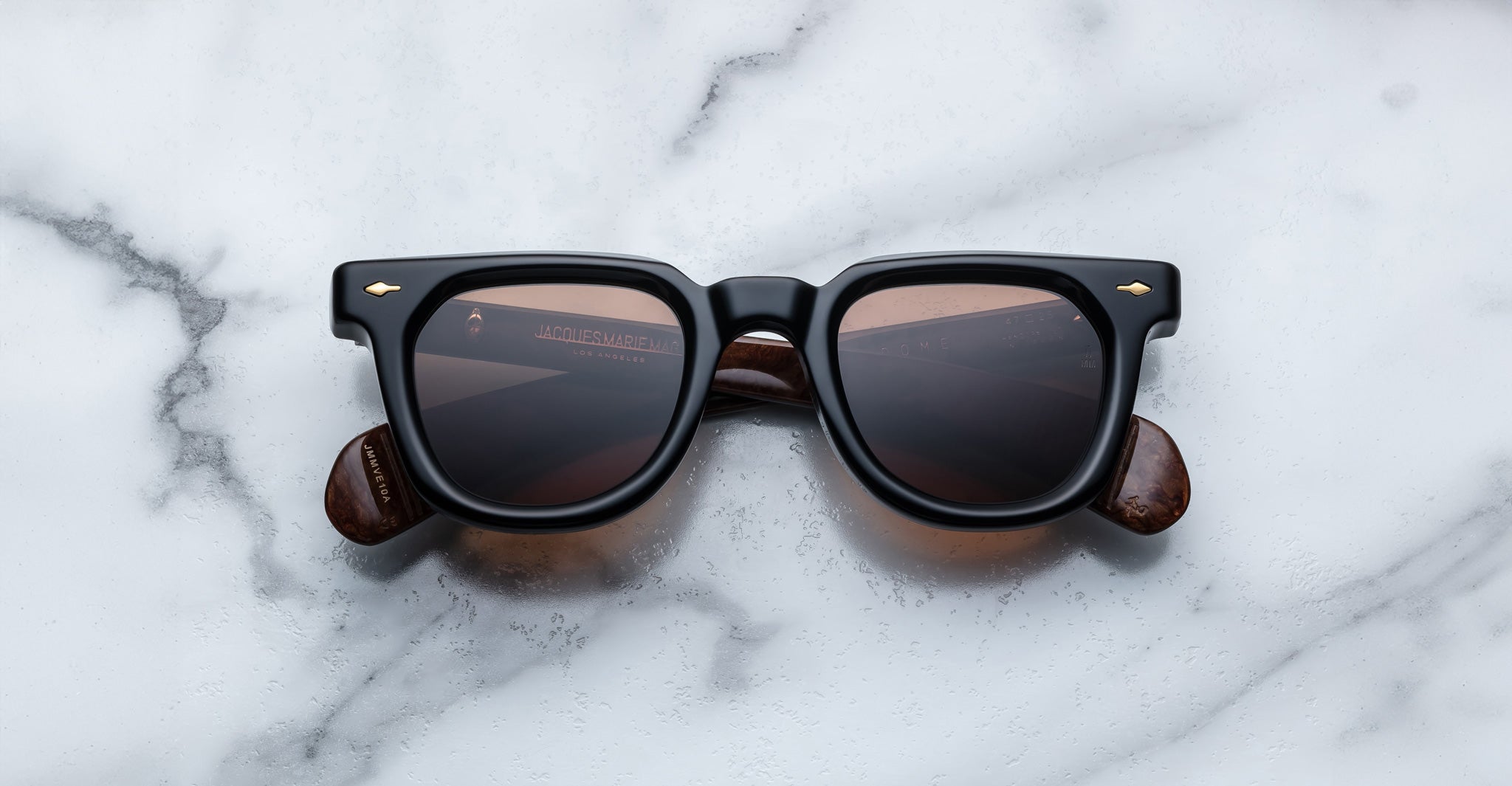 Jacques Marie Mage Vendome sunglasses by Jacques Marie Mage, featuring black square frames and dark lenses, handcrafted in Japan, are displayed on a white marble surface.