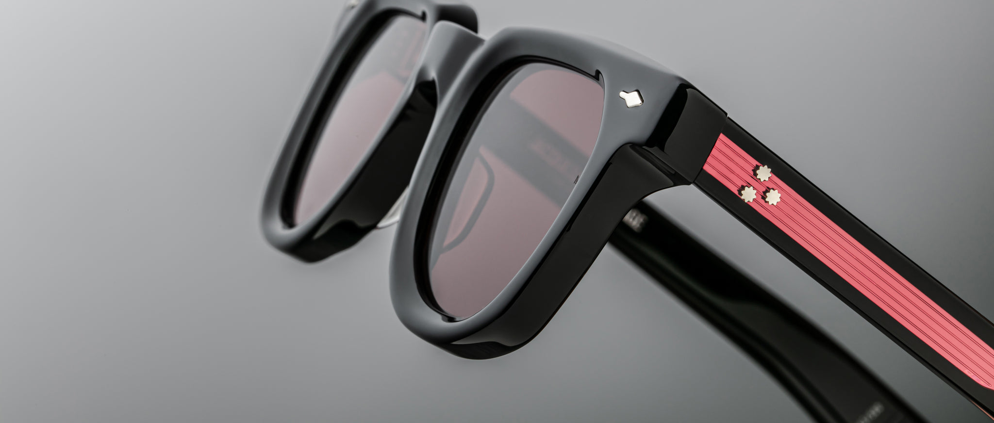 Close-up of Jacques Marie Mage Vendome sunglasses, black frame, dark lenses, pink stripe, and white flower detail on temples.