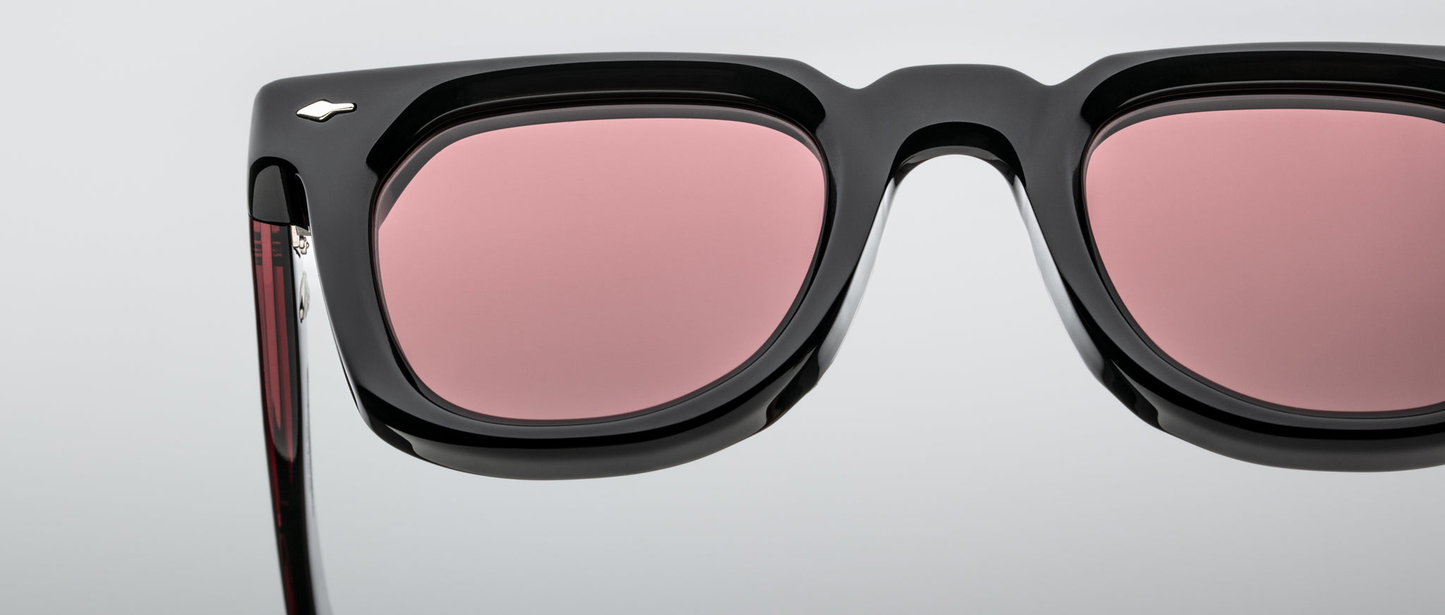 Close-up of Jacques Marie Mage Vendome sunglasses featuring a black frame, pink lenses, and a small silver logo on the temple.