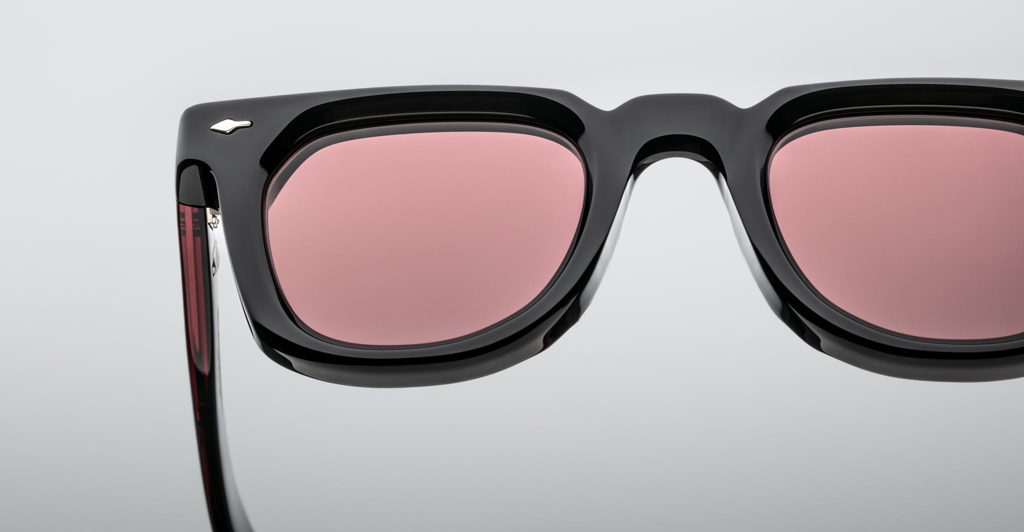 Close-up of Jacques Marie Mage Vendome sunglasses, featuring black frames and pink-tinted lenses, handcrafted in Japan, displayed on a plain light gray background.