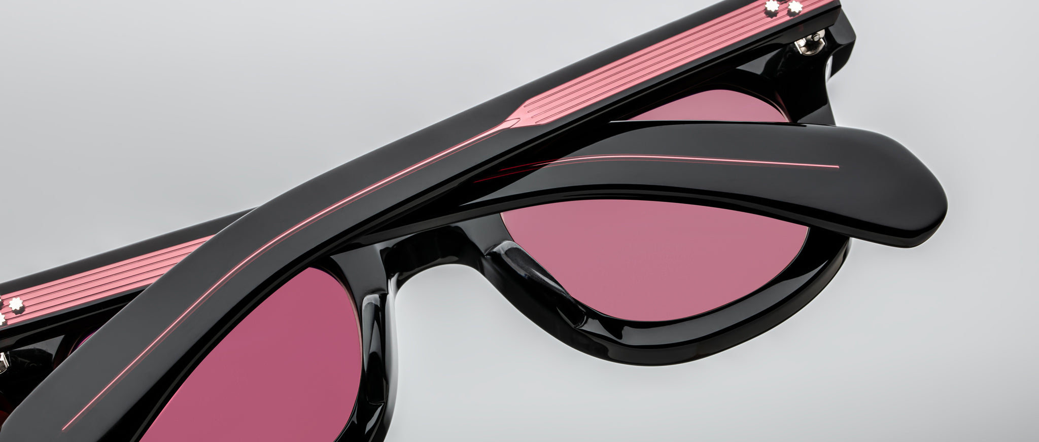 Close-up of Jacques Marie Mage Vendome sunglasses, black frame with pink-tinted lenses and a pink stripe accent.