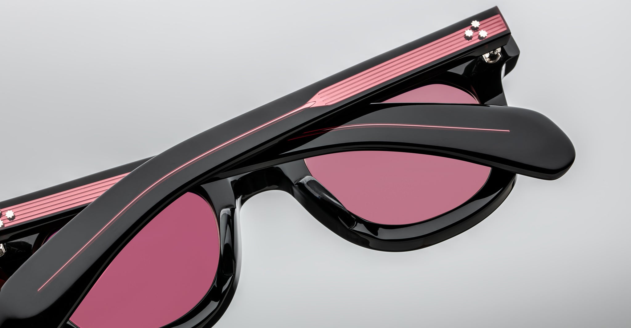 Close-up of folded Jacques Marie Mage Vendome sunglasses in black and pink with pink-tinted lenses, handcrafted in Japan, shown on a light background.