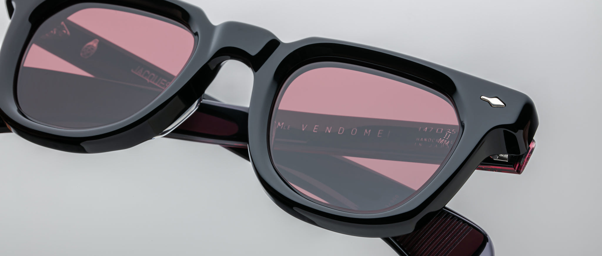 Close-up of Jacques Marie Mage Vendome sunglasses featuring black frames and rectangular pink lenses, viewed from the front.