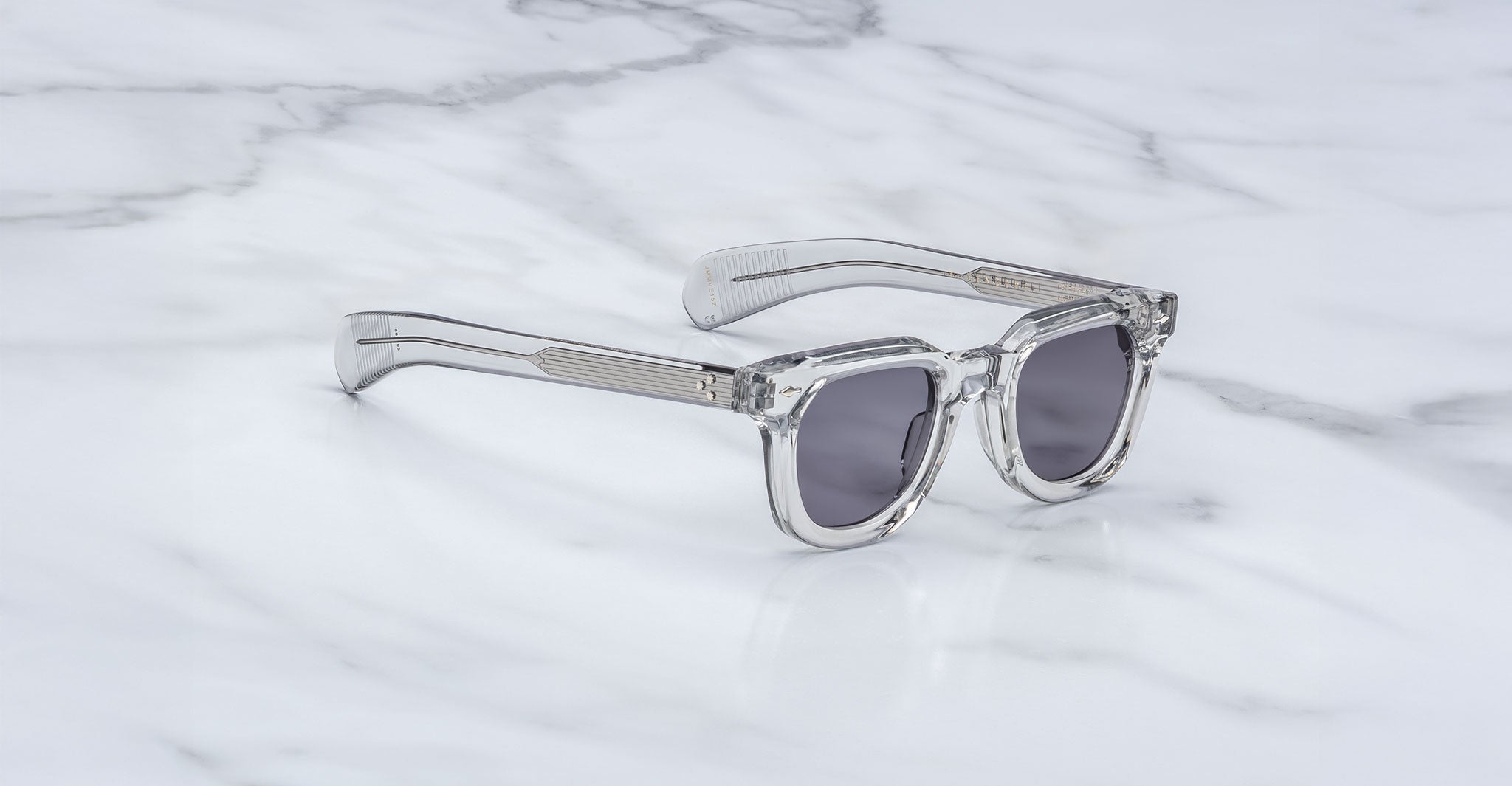 Jacques Marie Mage Vendome clear-frame sunglasses with dark lenses, handcrafted in Japan by Jacques Marie Mage, displayed on a white marble surface.