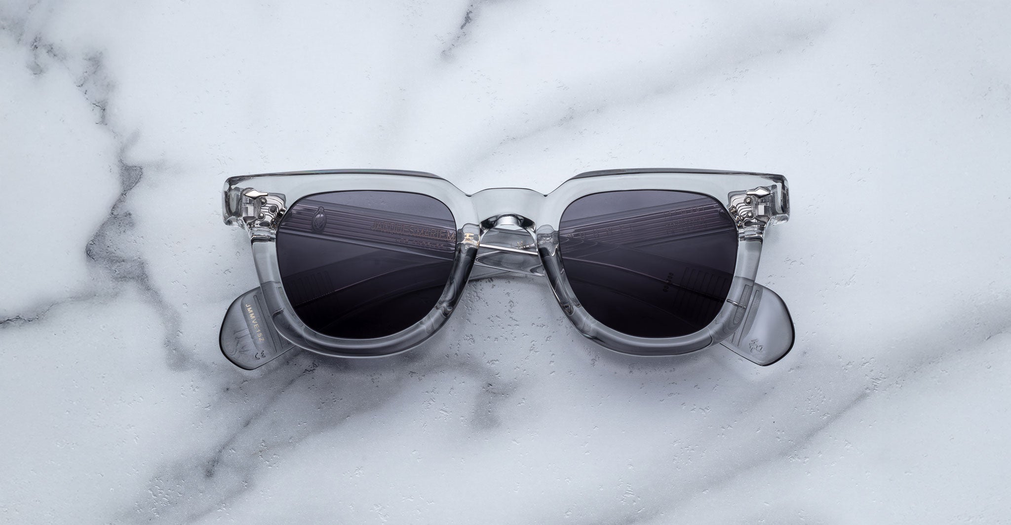 Jacques Marie Mage Vendome sunglasses featuring clear frames and dark lenses, from Jacques Marie Mage, displayed on a white marble surface.