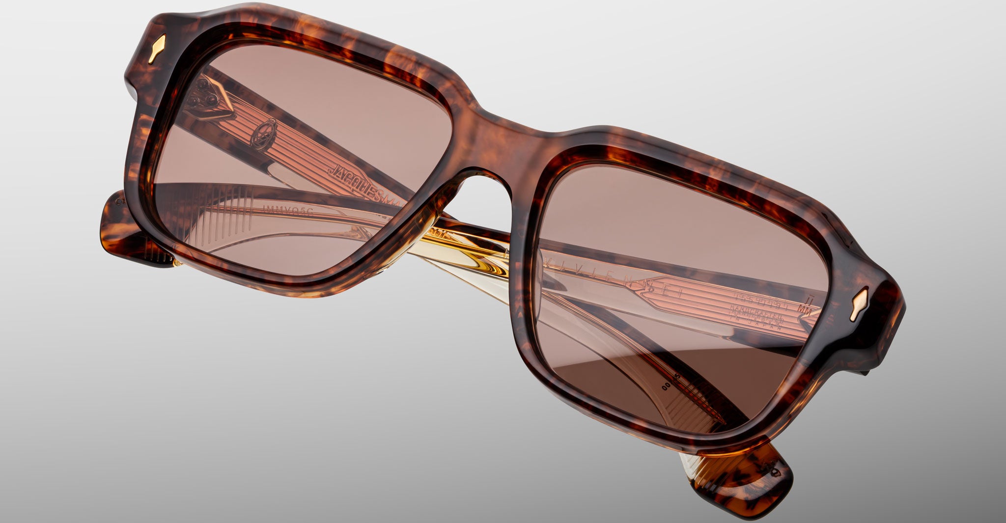 Close-up of stylish, rectangular tortoiseshell sunglasses with brown-tinted lenses, gold detailing on the inner arms, and a minimalist, light gray background.