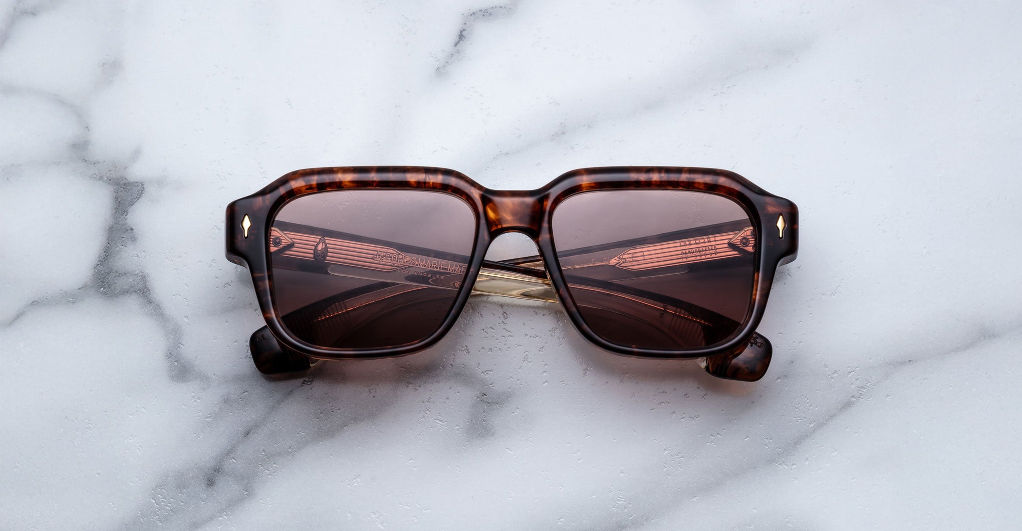 Brown tortoiseshell square sunglasses with dark lenses, placed on a white marble surface.