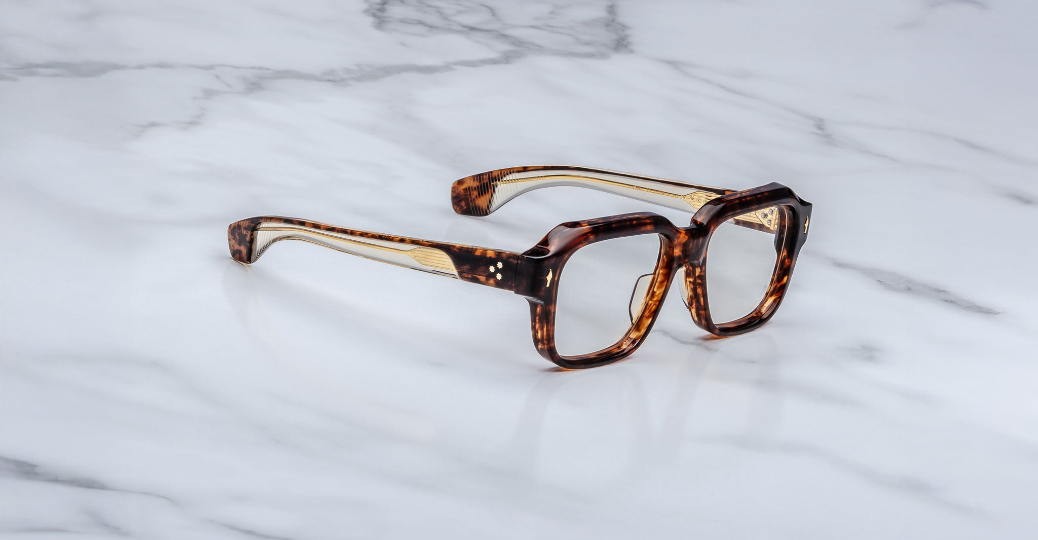 Jacques Marie Mage Vivienne square eyeglasses with thick tortoiseshell frames are shown on a white marble surface, angled to display both the front and one side of the frames.