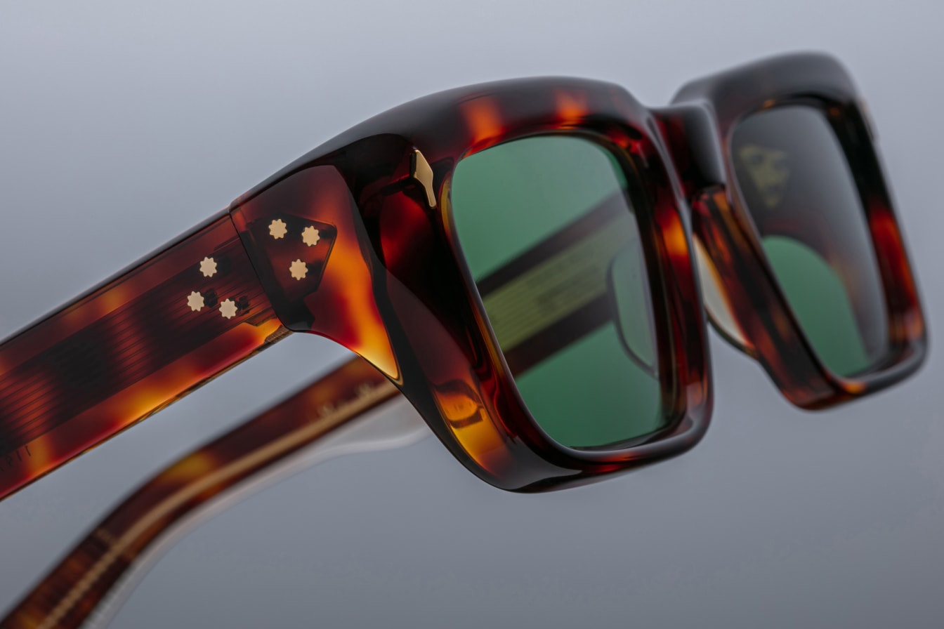 Close-up of Jacques Marie Mage Walker sunglasses showing green lenses and a crest detail on the temple.
