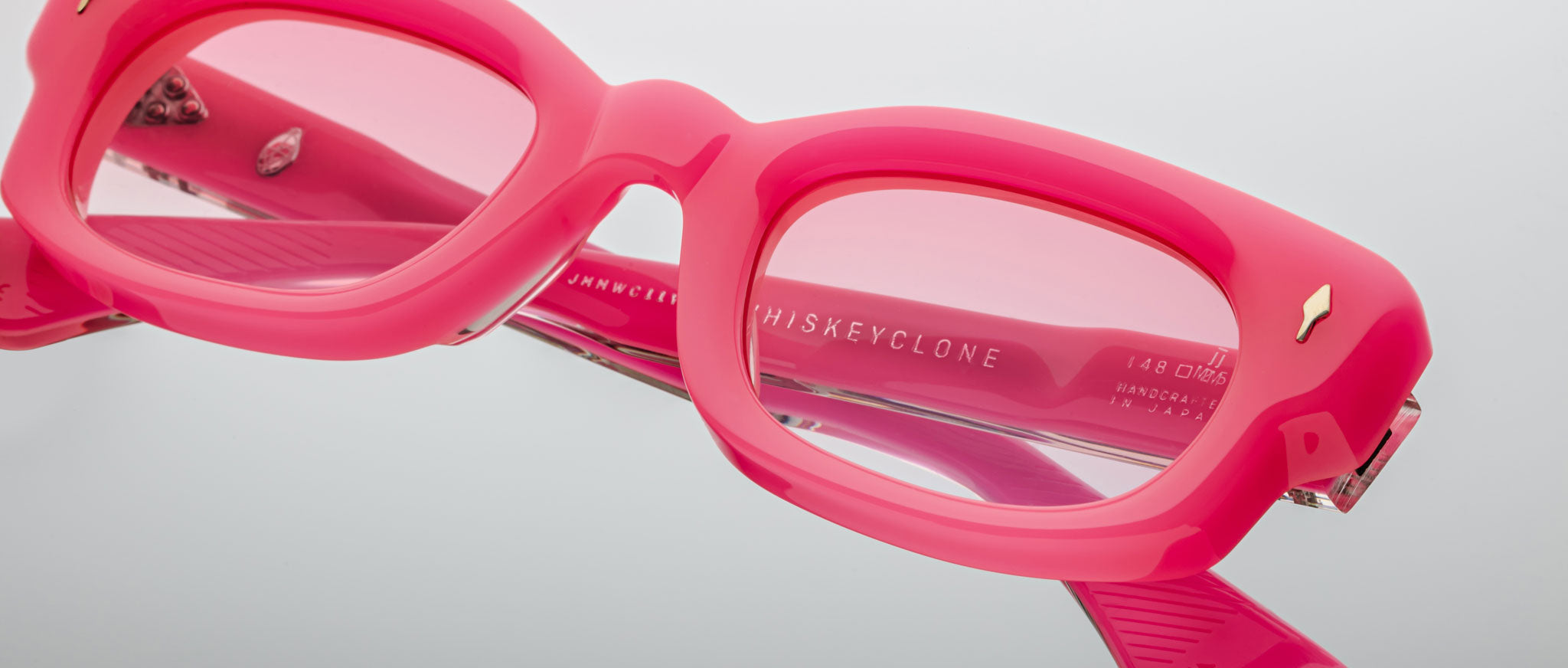 Close-up view of Jacques Marie Mage Whiskeyclone eyeglasses—thick, rectangular frames in bright pink with pink-tinted lenses—shown on a white background. Brand and model details are visible inside the frame.