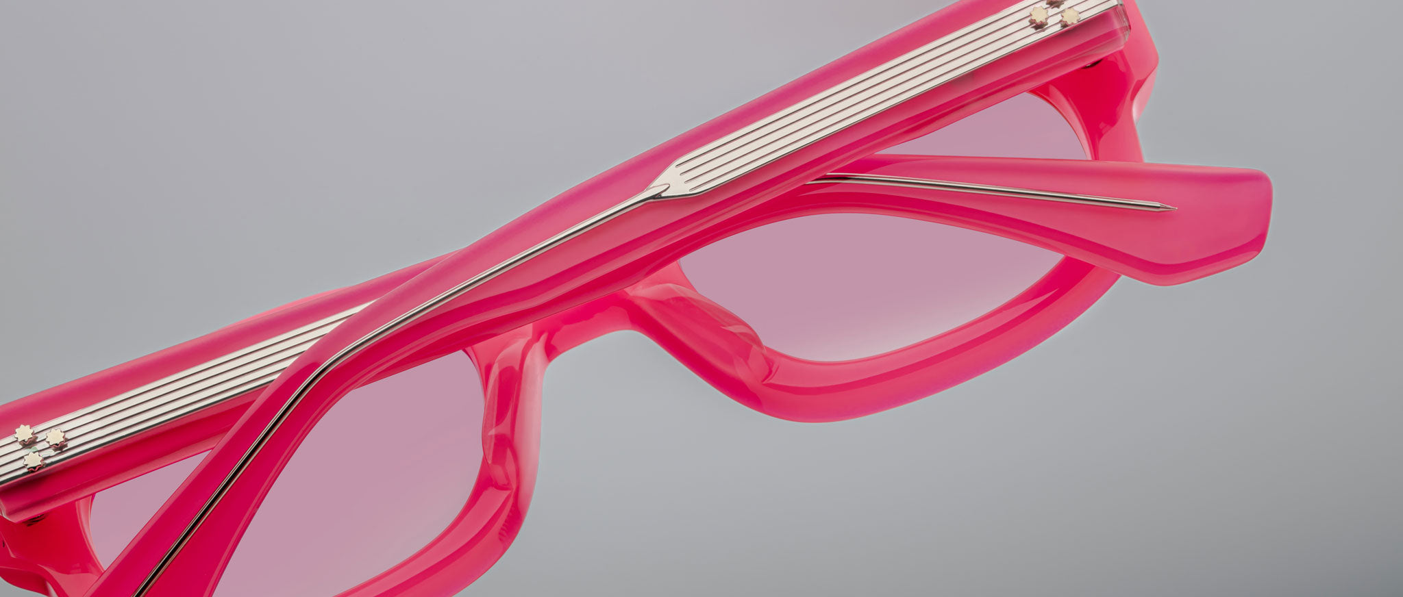 A close-up of Jacques Marie Mage Whiskeyclone sunglasses with bright pink, pink-tinted lenses and metallic arm detailing, set against a plain light gray background.