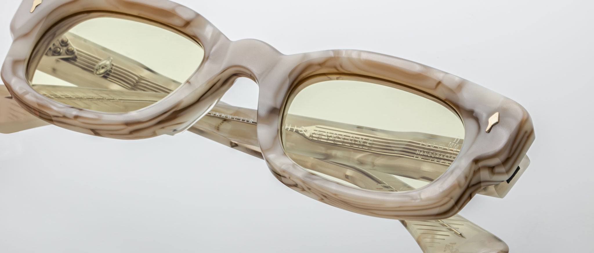 Close-up of Jacques Marie Mage Whiskeyclone rectangular eyeglasses with thick marbled beige and brown frames, light yellow-tinted lenses, isolated on a plain white background.