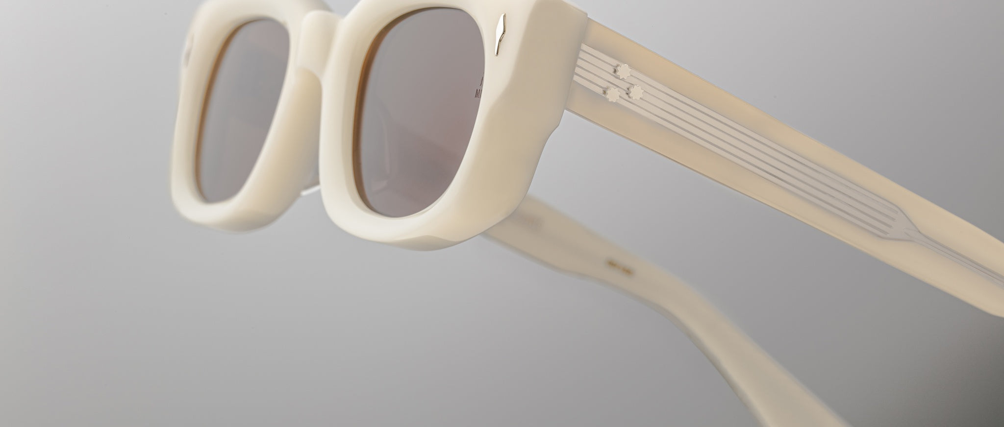 Close-up of Jacques Marie Mage Whiskeyclone sunglasses featuring stylish, chunky white frames and gray-tinted lenses, set against a plain light background.