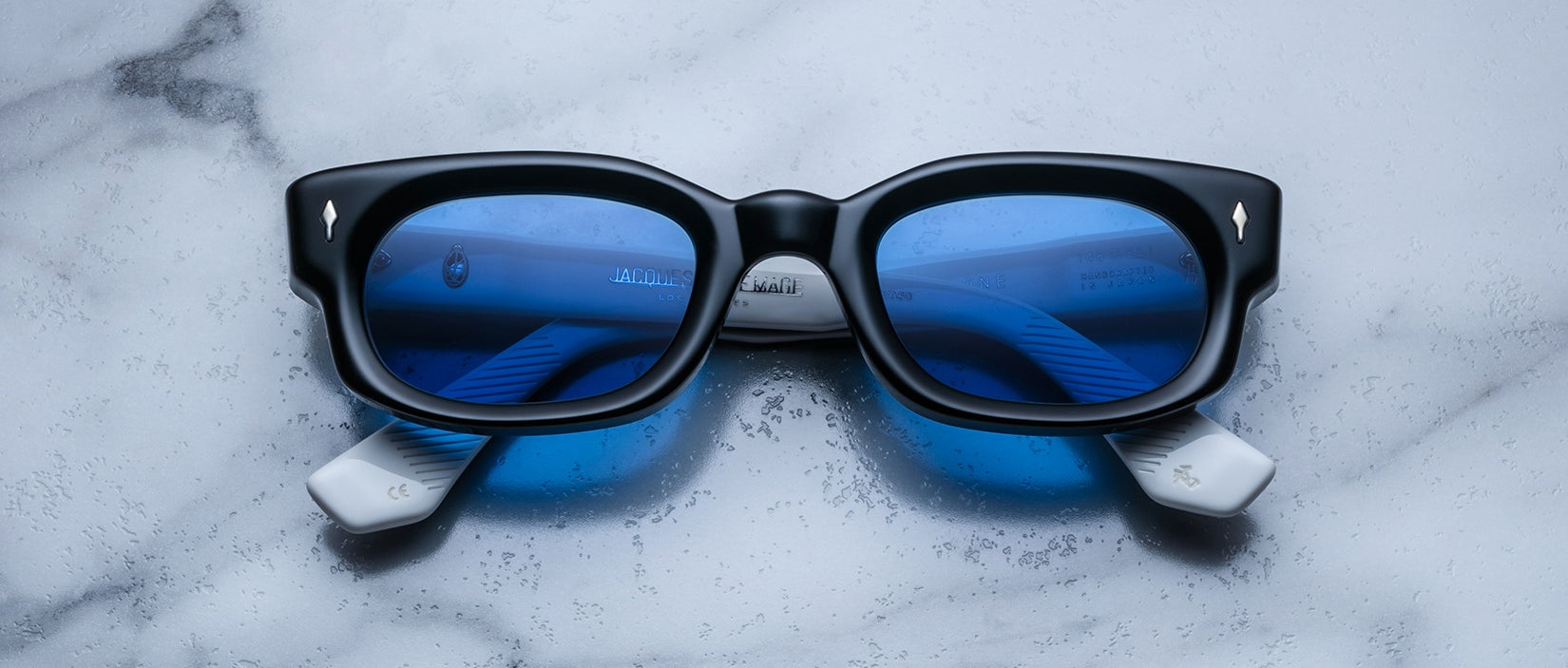 Jacques Marie Mage Whiskeyclone sunglasses, blue-tinted lenses, white arms, top view.