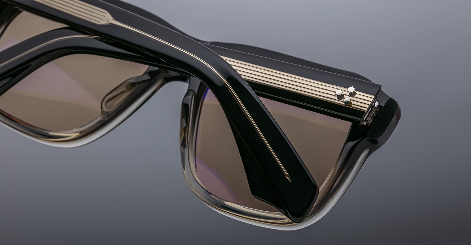 Close-up of Jacques Marie Mage Yves sunglasses, black frame with gold rim and tinted lenses, shown from the front angle.