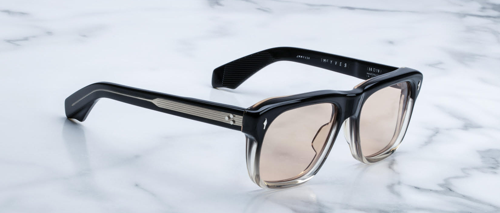 Jacques Marie Mage Yves sunglasses featuring black and translucent frames with light brown lenses, viewed from above.