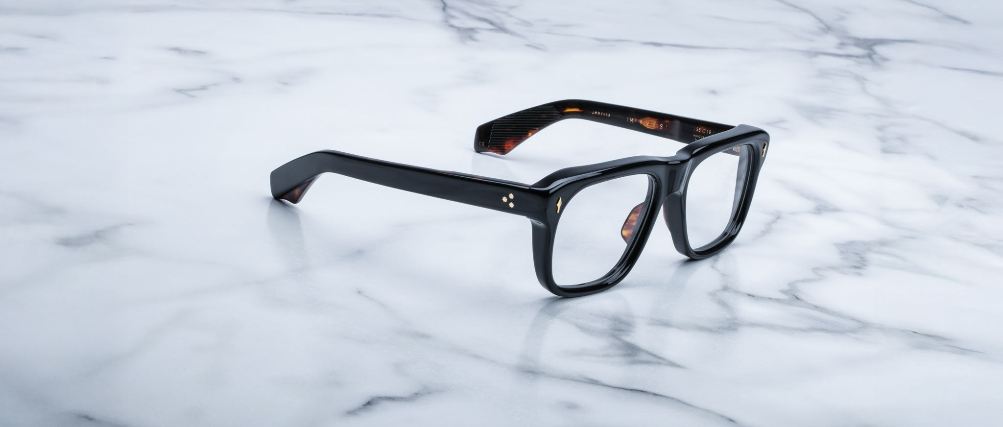 Jacques Marie Mage Yves in Noir 15 optical, rectangular black acetate frame with subtle tortoise interior, clear lenses, and signature arrowhead rivet detail, shown in angled side view on marble surface