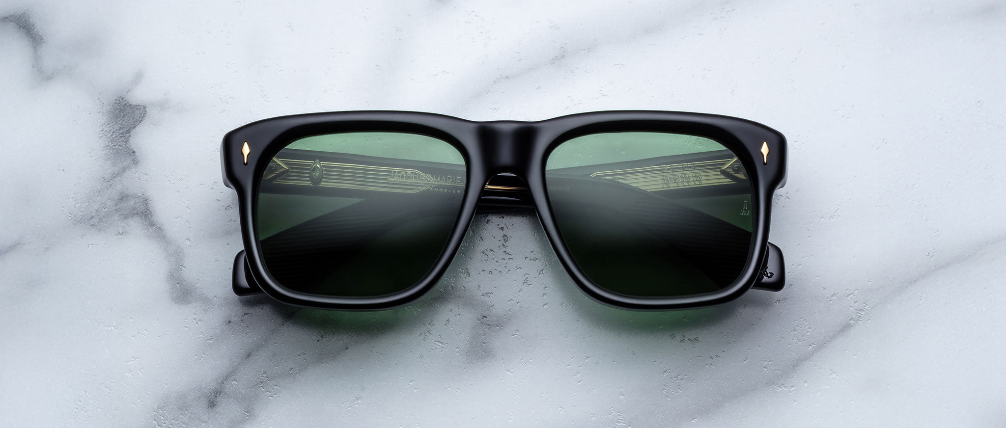 Jacques Marie Mage Yves sunglasses with green-tinted lenses, viewed from above, reflect a car dashboard.