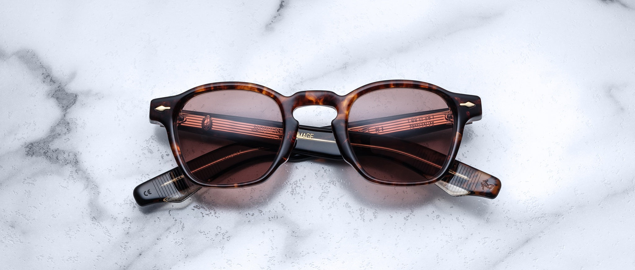 Jacques Marie Mage Zephirin sunglasses in brown tortoiseshell with dark lenses rest closed on white marble, highlighting the exclusivity of this limited edition eyewear.