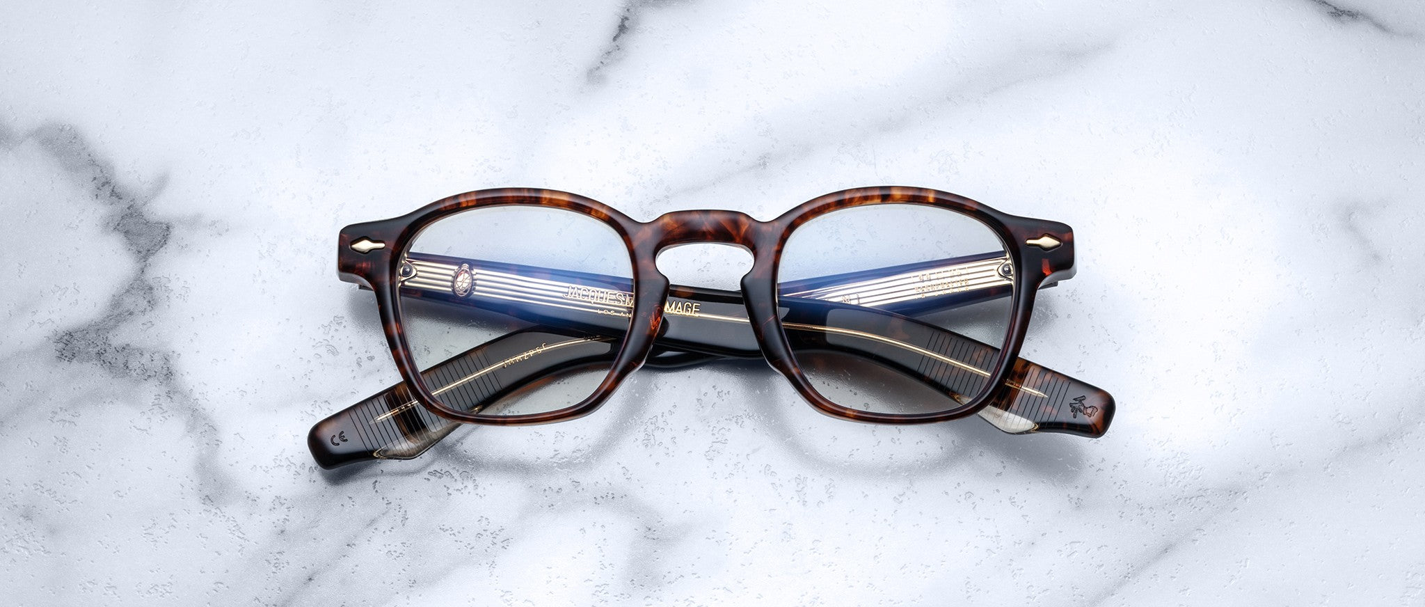 A pair of Jacques Marie Mage Zephirin spectacles is folded and displayed on a white marble surface.