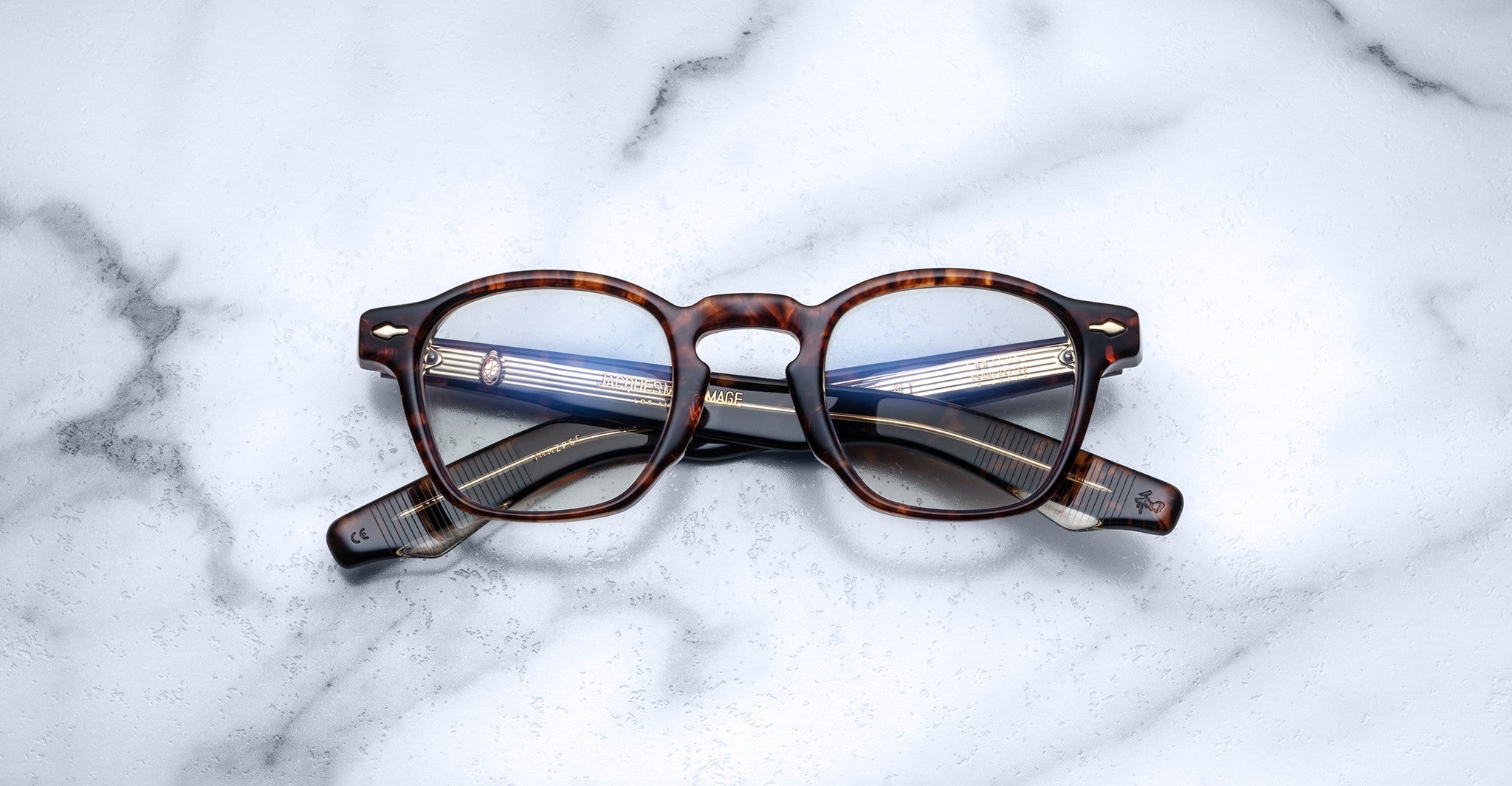 A pair of Jacques Marie Mage Zephirin spectacles is folded and displayed on a white marble surface.