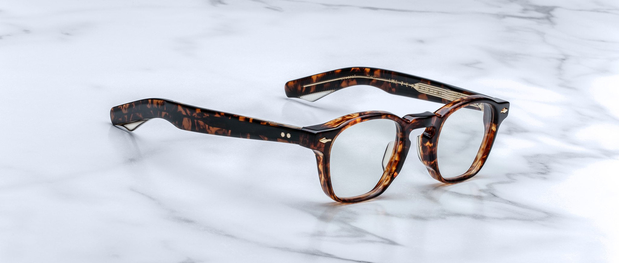 Jacques Marie Mage Zephirin spectacles by Jacques Marie Mage feature handcrafted acetate, round lenses, and a tortoiseshell finish, displayed on white marble to highlight the refined appeal of this limited edition eyewear.