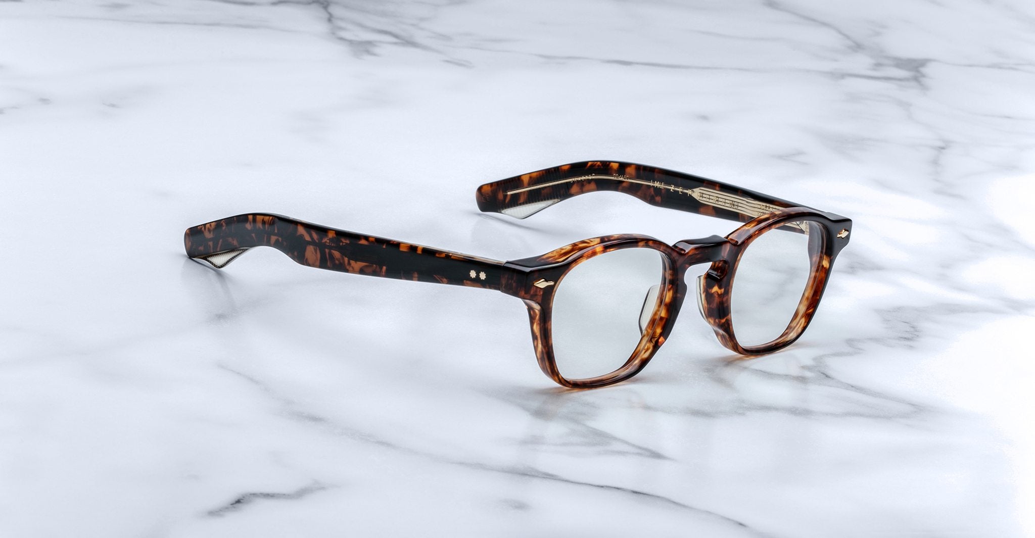 Jacques Marie Mage Zephirin spectacles by Jacques Marie Mage feature handcrafted acetate, round lenses, and a tortoiseshell finish, displayed on white marble to highlight the refined appeal of this limited edition eyewear.